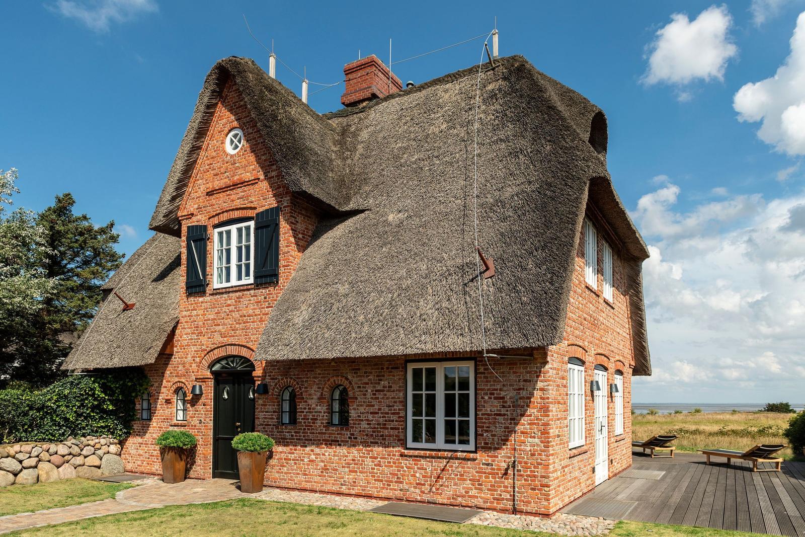 Rotes Backsteinhaus mit Strohdach und Terrasse am Meer.