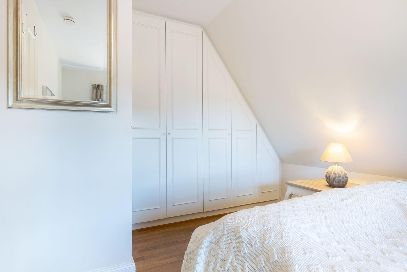 Bedroom with white wardrobe, mirror, and bedside table with lamp.