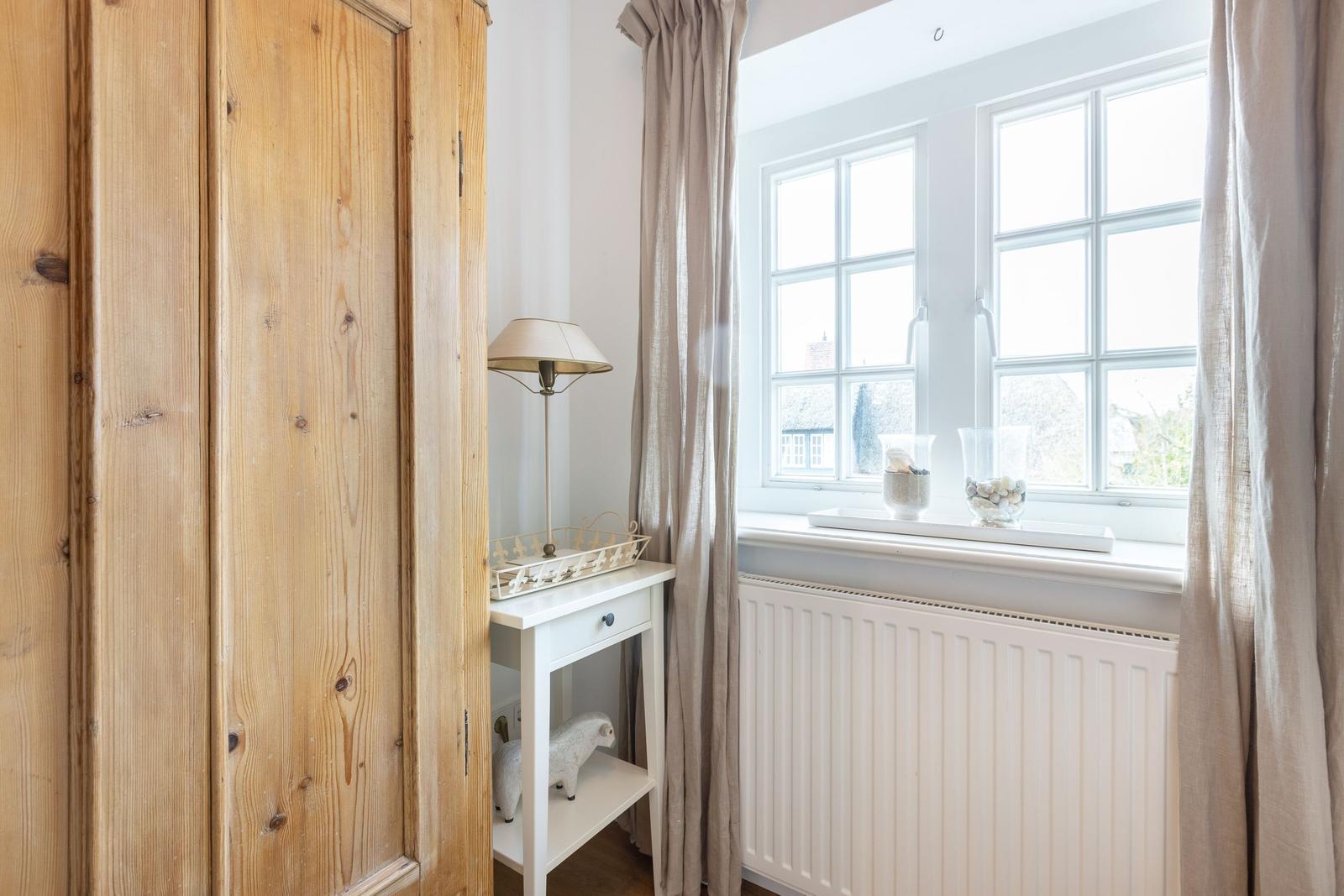A room with wooden wardrobe, white cabinet, and window with curtains.