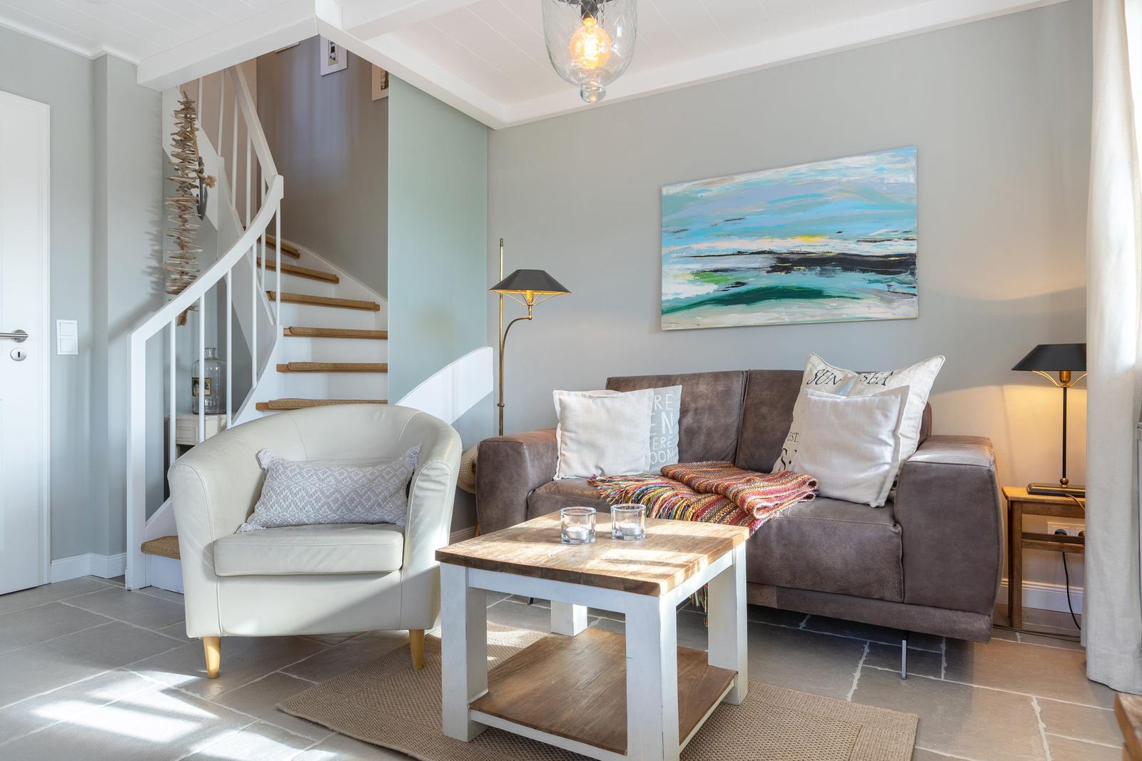 Living room with sofa, armchair, table, and wall art. Staircase in the background.