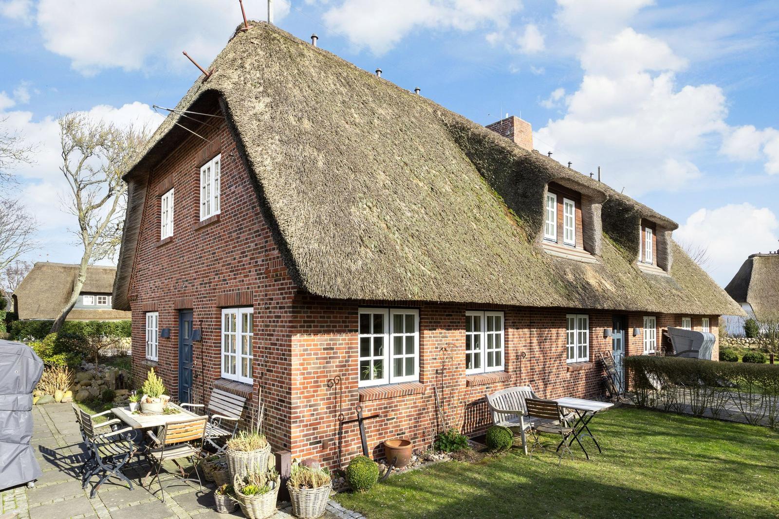 Red brick house with thatched roof and garden area with tables and chairs.