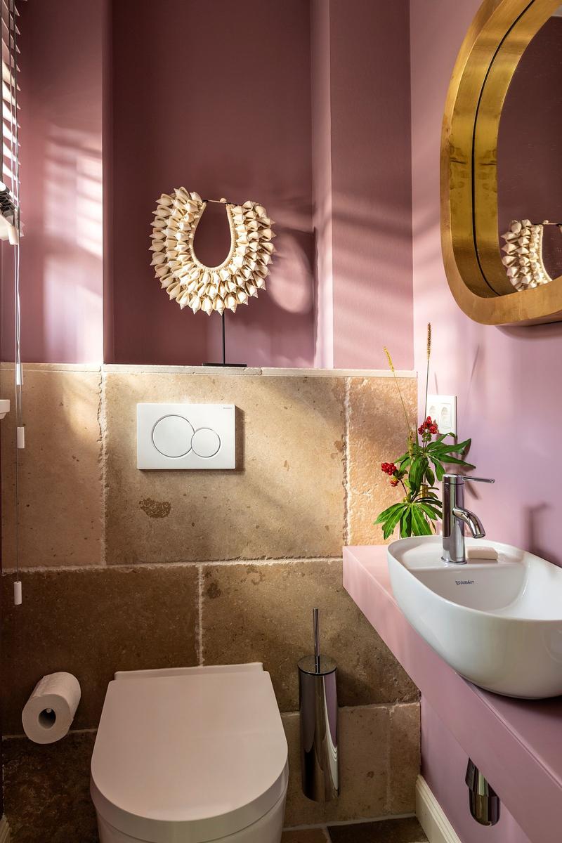 Bad mit rosa Wänden, Waschbecken und Toilette. Goldrand-Spiegel und Dekoration.