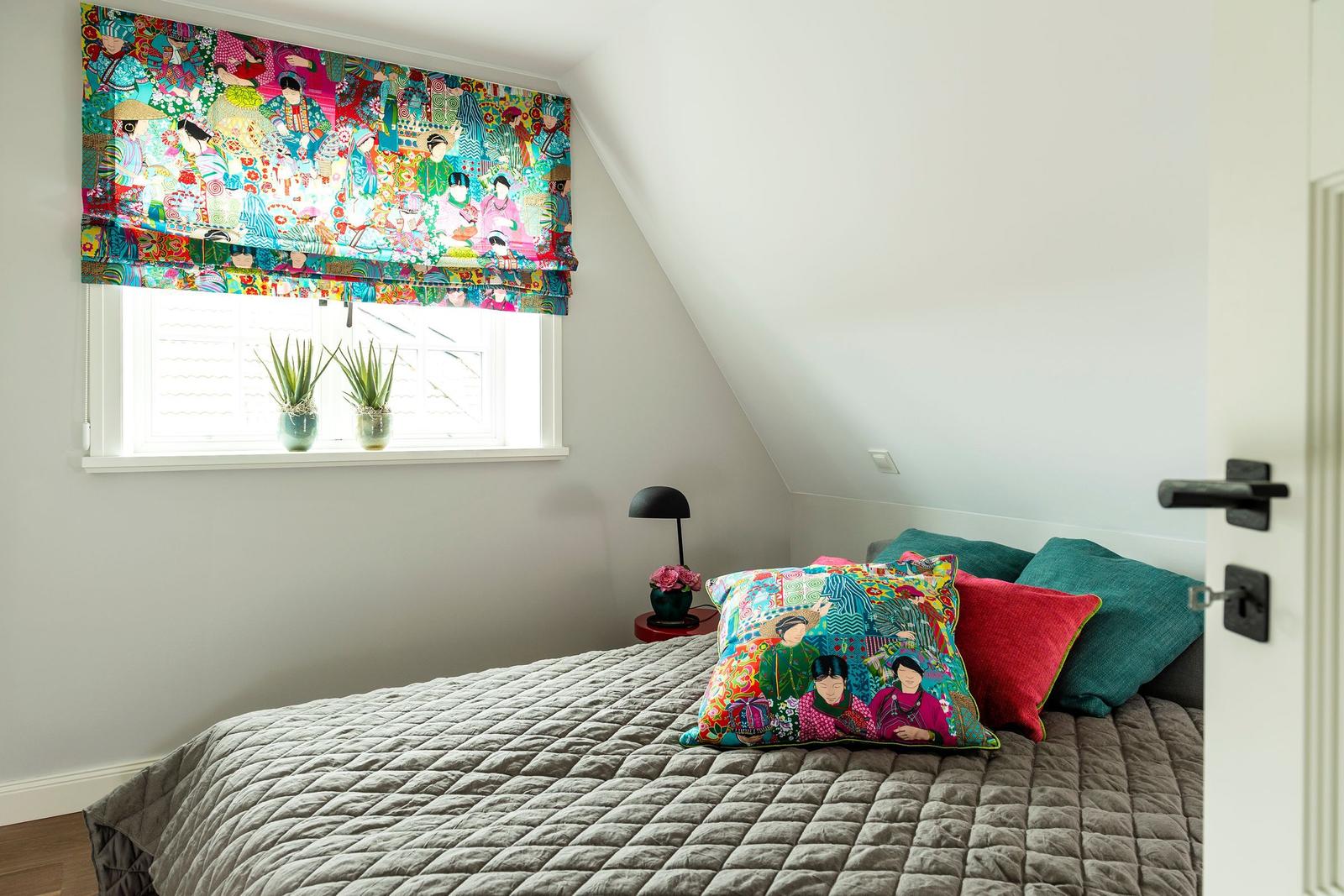 Schlafzimmer mit Bett, Fenster und bunten Vorhängen und Kissen.