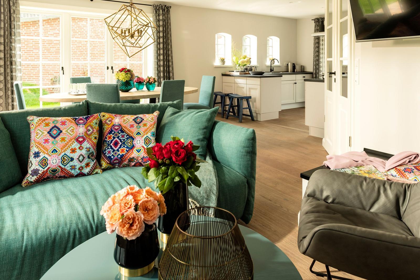 Wohnzimmer mit grünem Sofa, Blumen und Blick in die Küche.