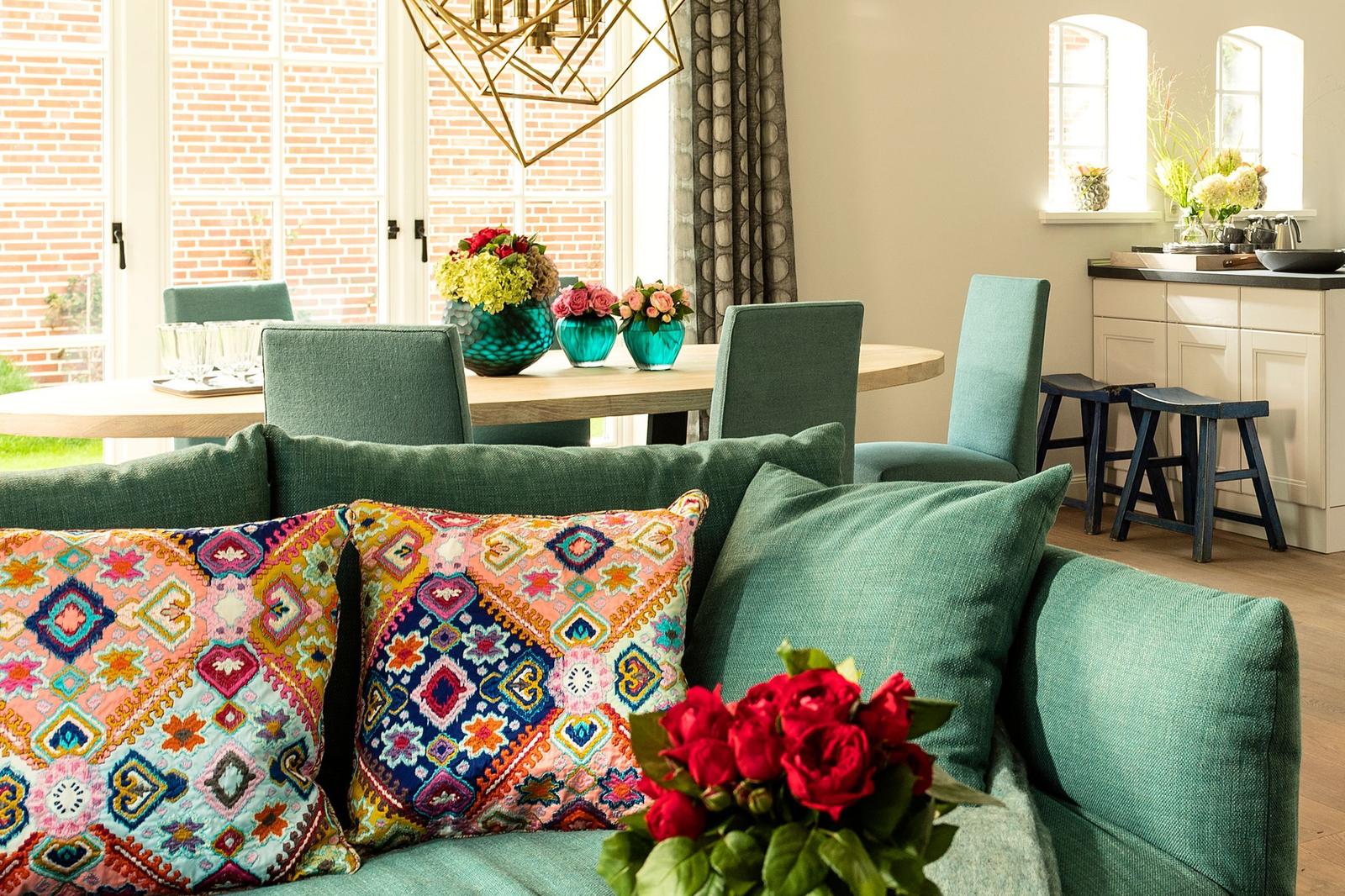 Ein Wohnzimmer mit grünem Sofa, bunten Kissen und Blumenarrangements.