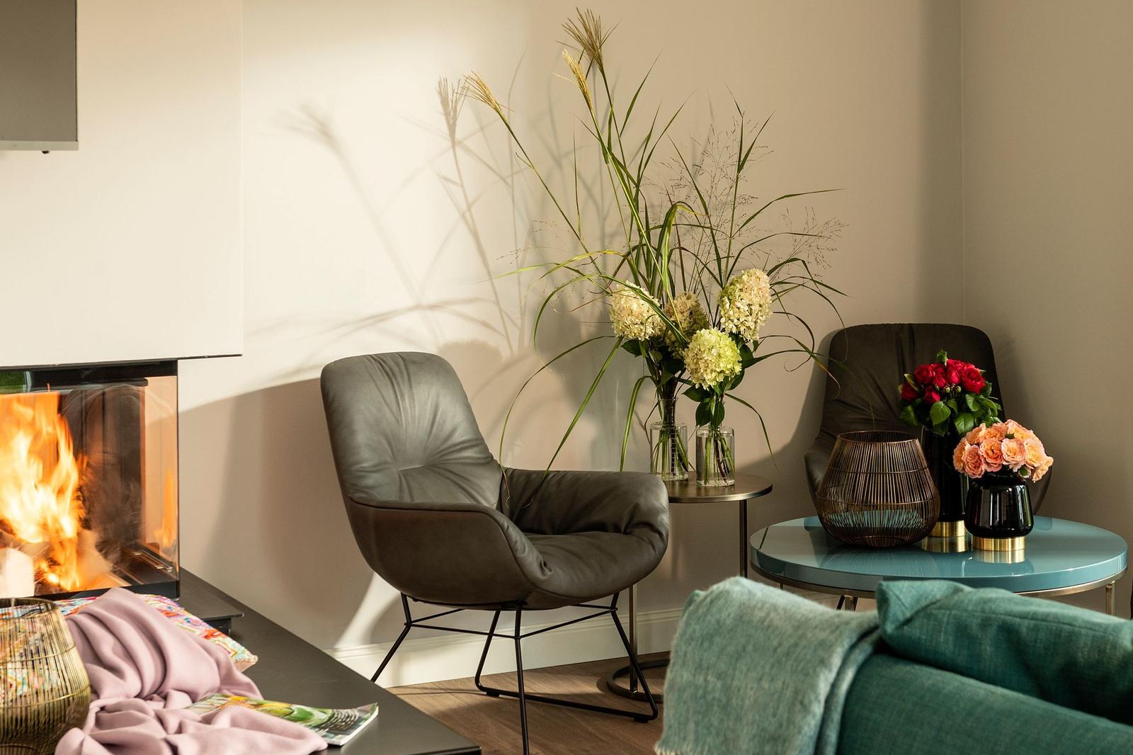 Ein Wohnzimmer mit Kamin, zwei Sesseln und Blumenarrangements auf Tischen.