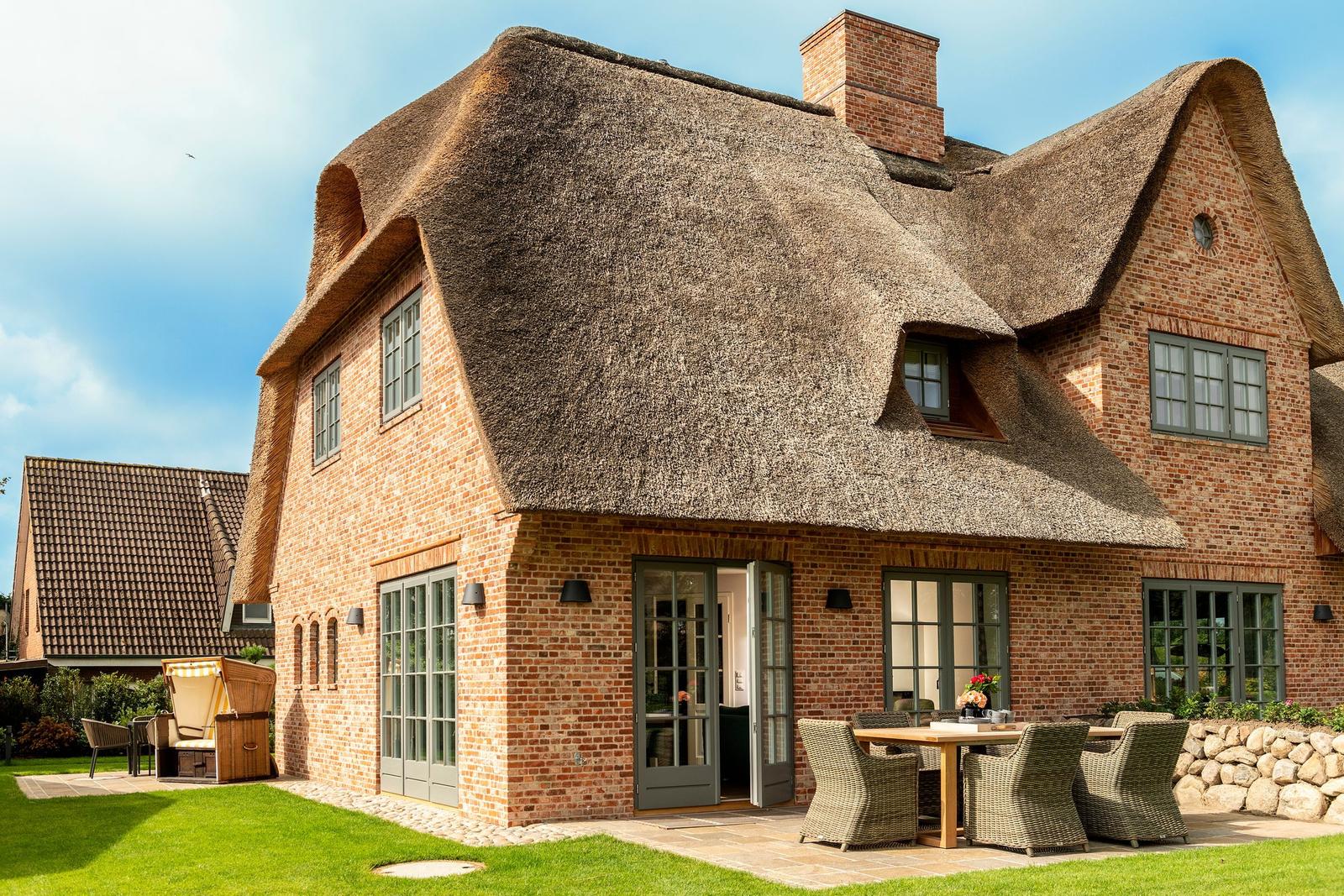 Haus mit strohgedecktem Dach und Steinmauer. Außenbereich mit Tisch und Stühlen.