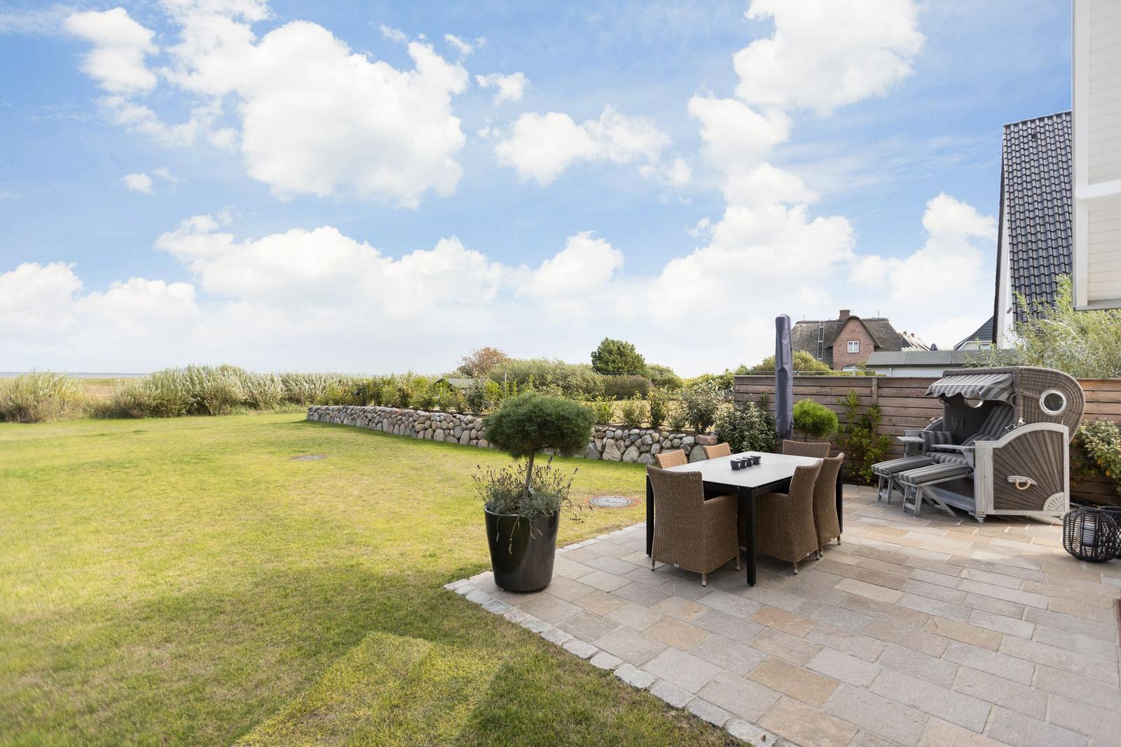 Terrasse mit Sitzgruppe und Blick auf Grünfläche und Himmel.