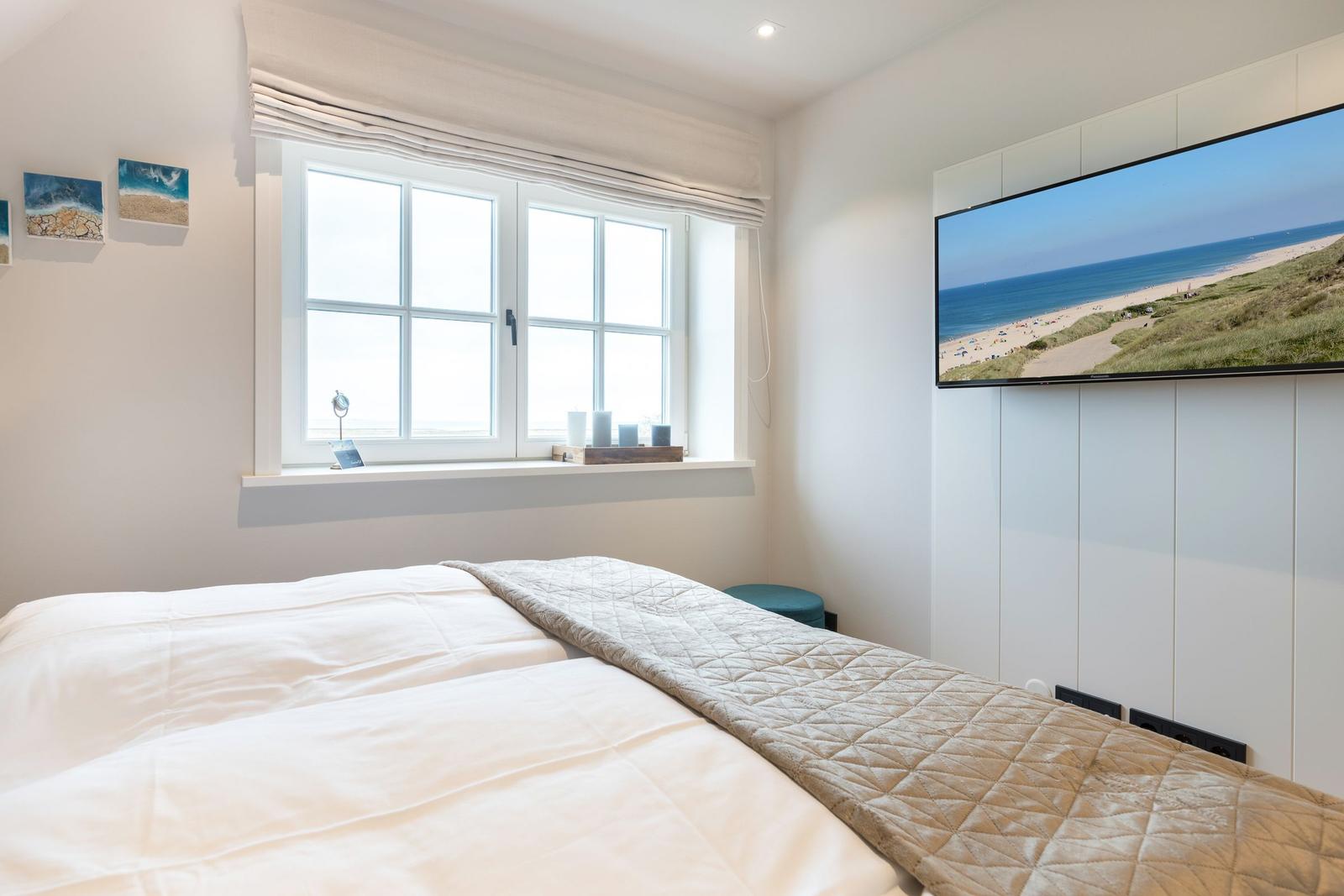 Schlafzimmer mit Bett, Fenster und Fernseher an der Wand.