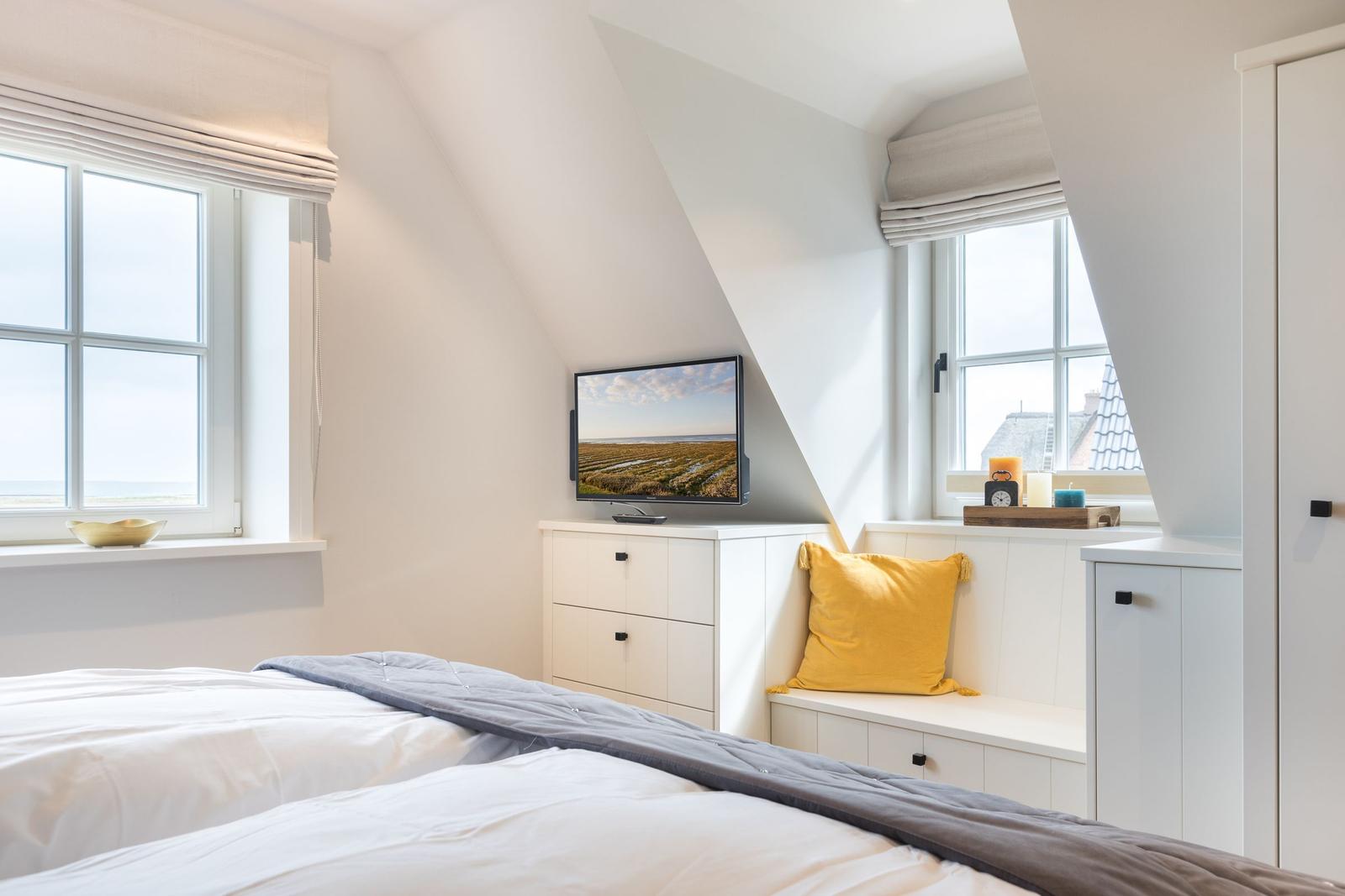 Schlafzimmer mit Dachschrägen, Fenstern, Bett und Fernseher.