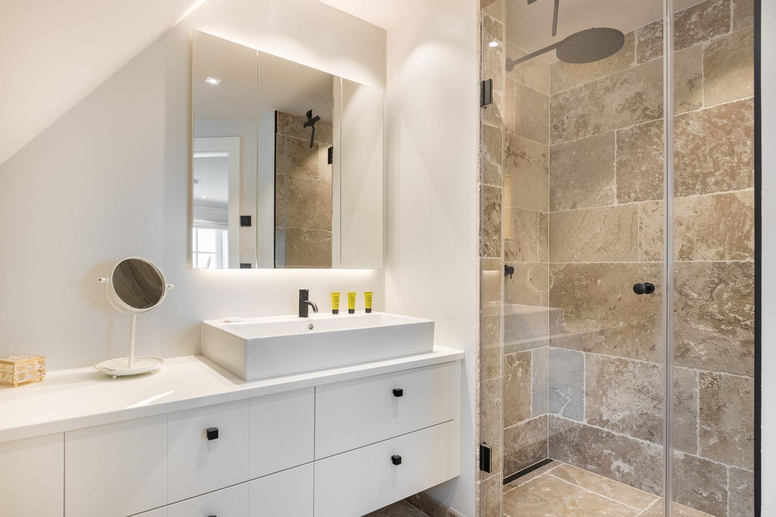 Badezimmer mit Waschtisch, Spiegel und Dusche mit Steinwand