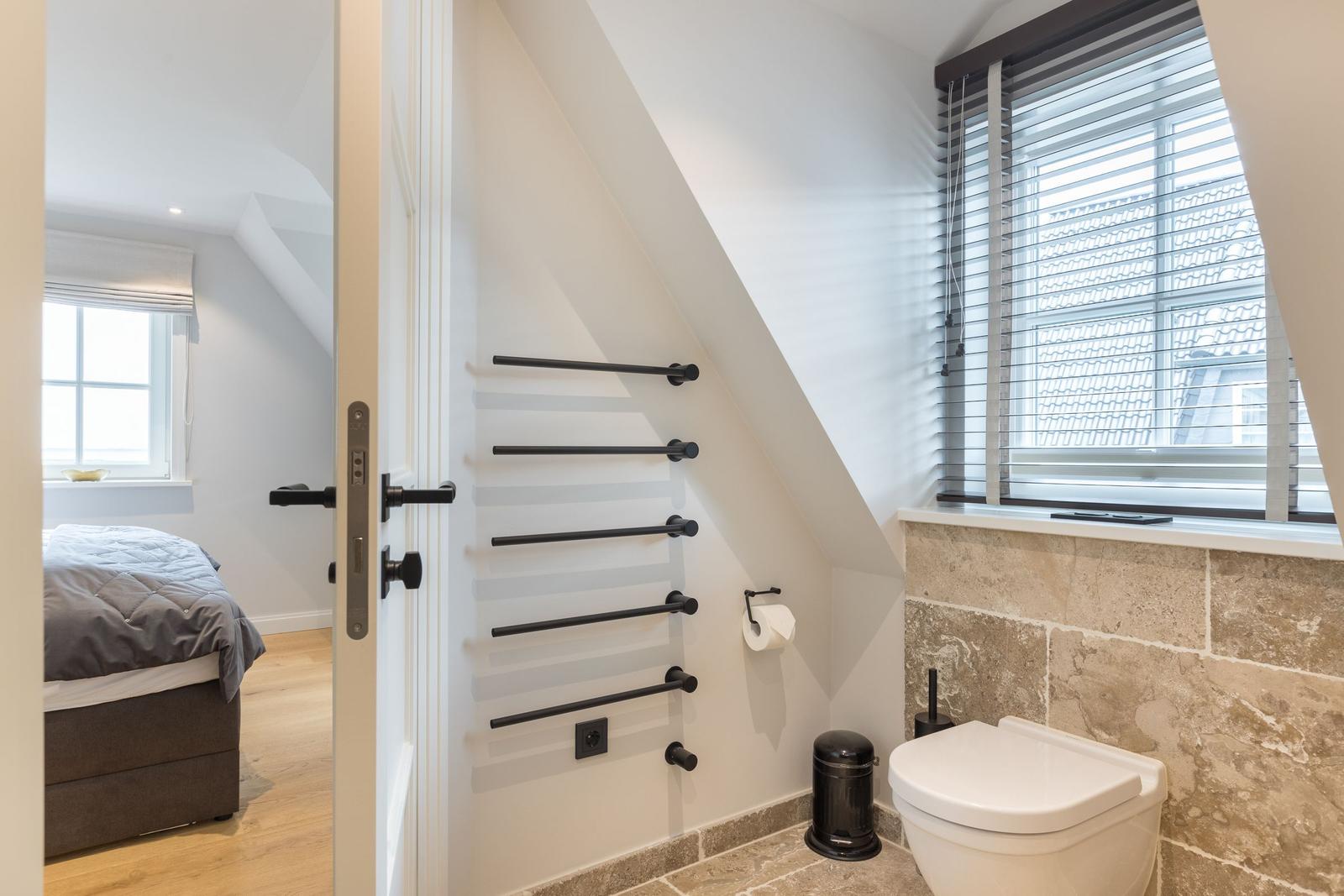 Badezimmer mit Toilette und Fenster. Tür führt in Schlafzimmer.