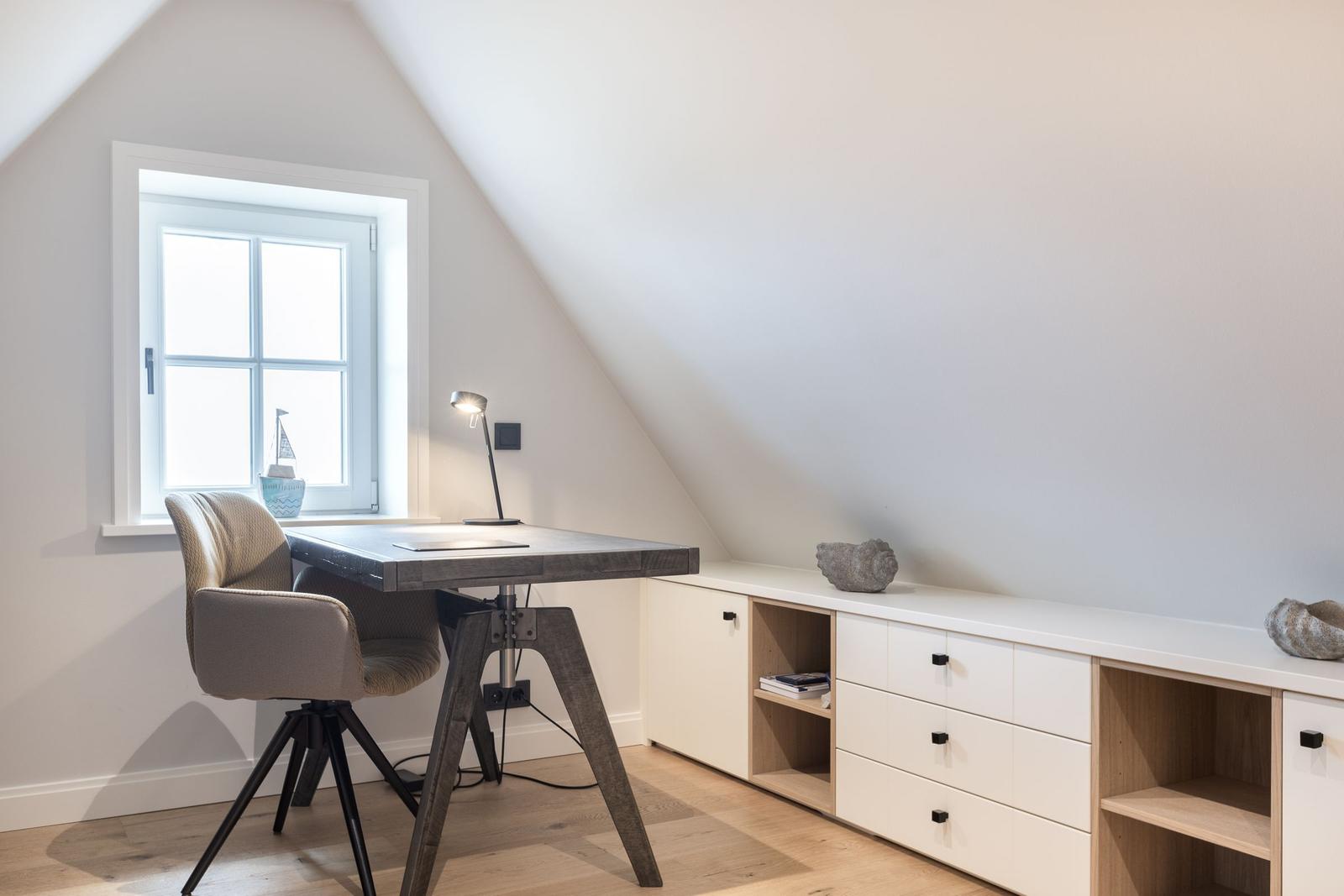 Arbeitsplatz mit Tisch, Stuhl und Schreibtischlampe unter Dachschrägenfenster.