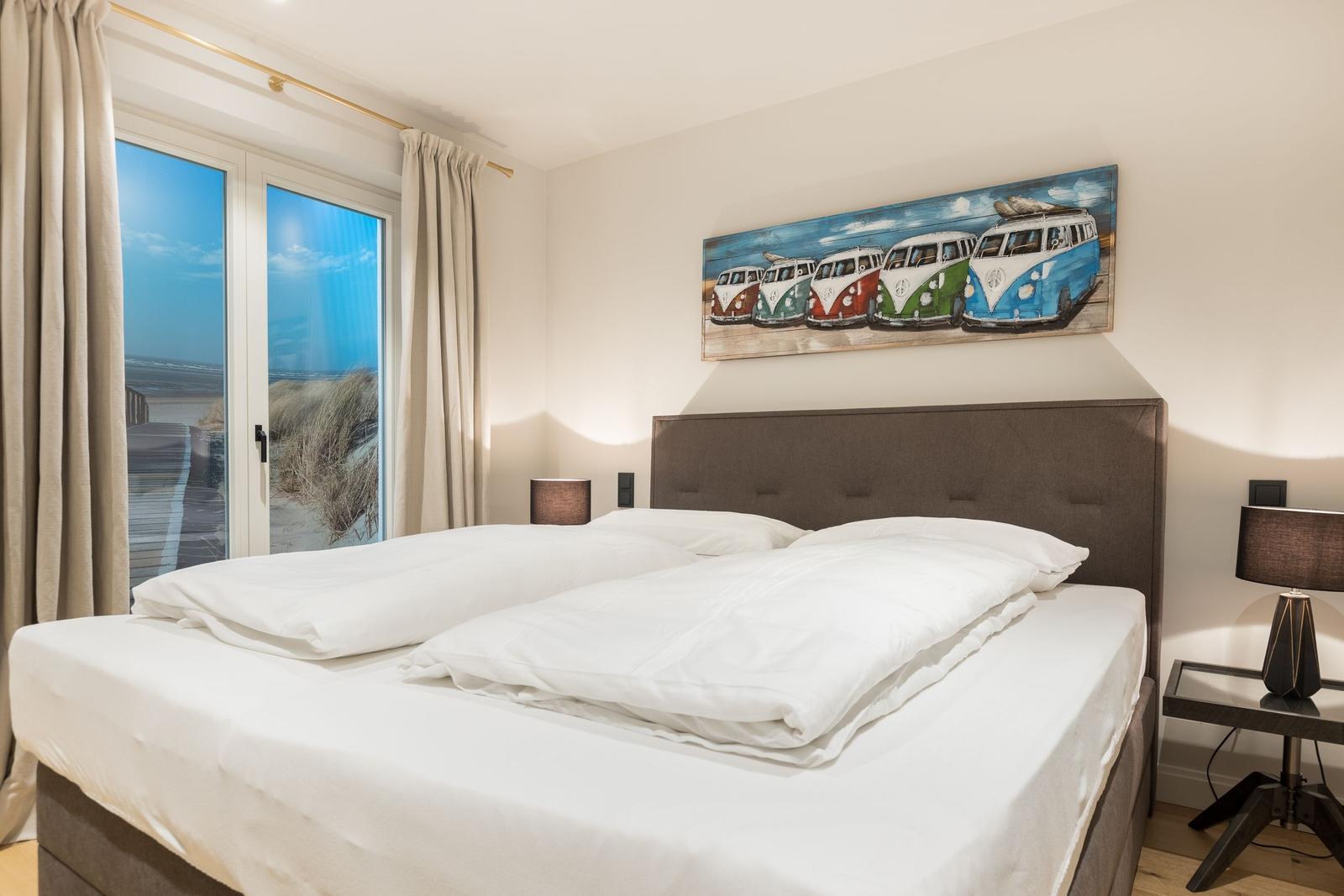 Schlafzimmer mit Bett, Fenster und Wandbild von VW-Bussen.