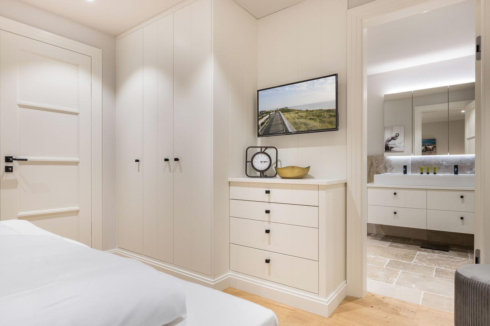 Schlafzimmer mit Kleiderschrank, TV und Blick in das Badezimmer.