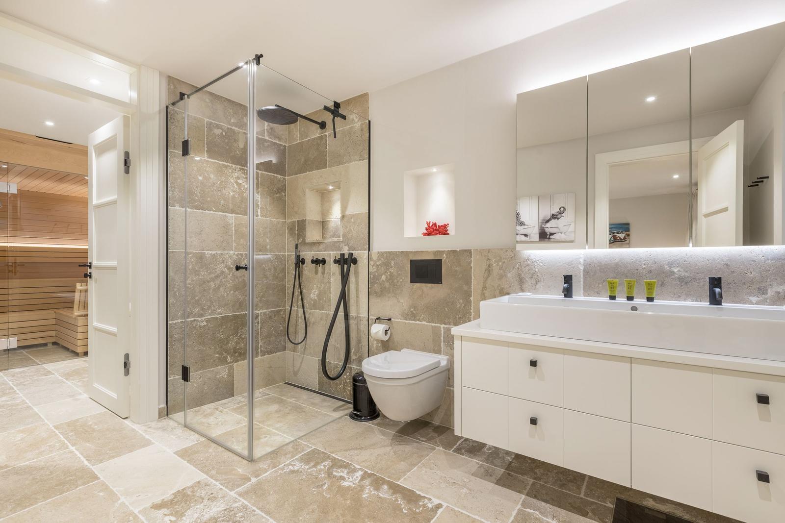 Bad mit Dusche, Waschbecken und Toilette. Sauna ist im Hintergrund sichtbar.