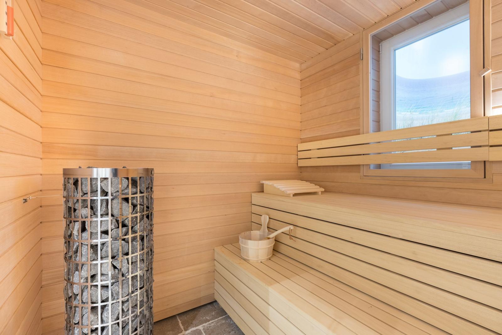 Sauna mit Holzbank, Steinofen und Fensterblick auf Strand