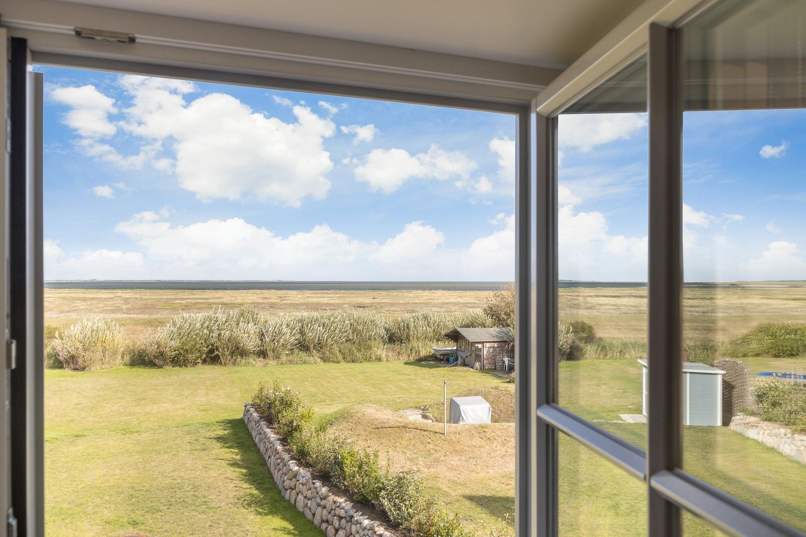 Blick aus dem Fenster auf Grasland und Himmel mit Wolken.