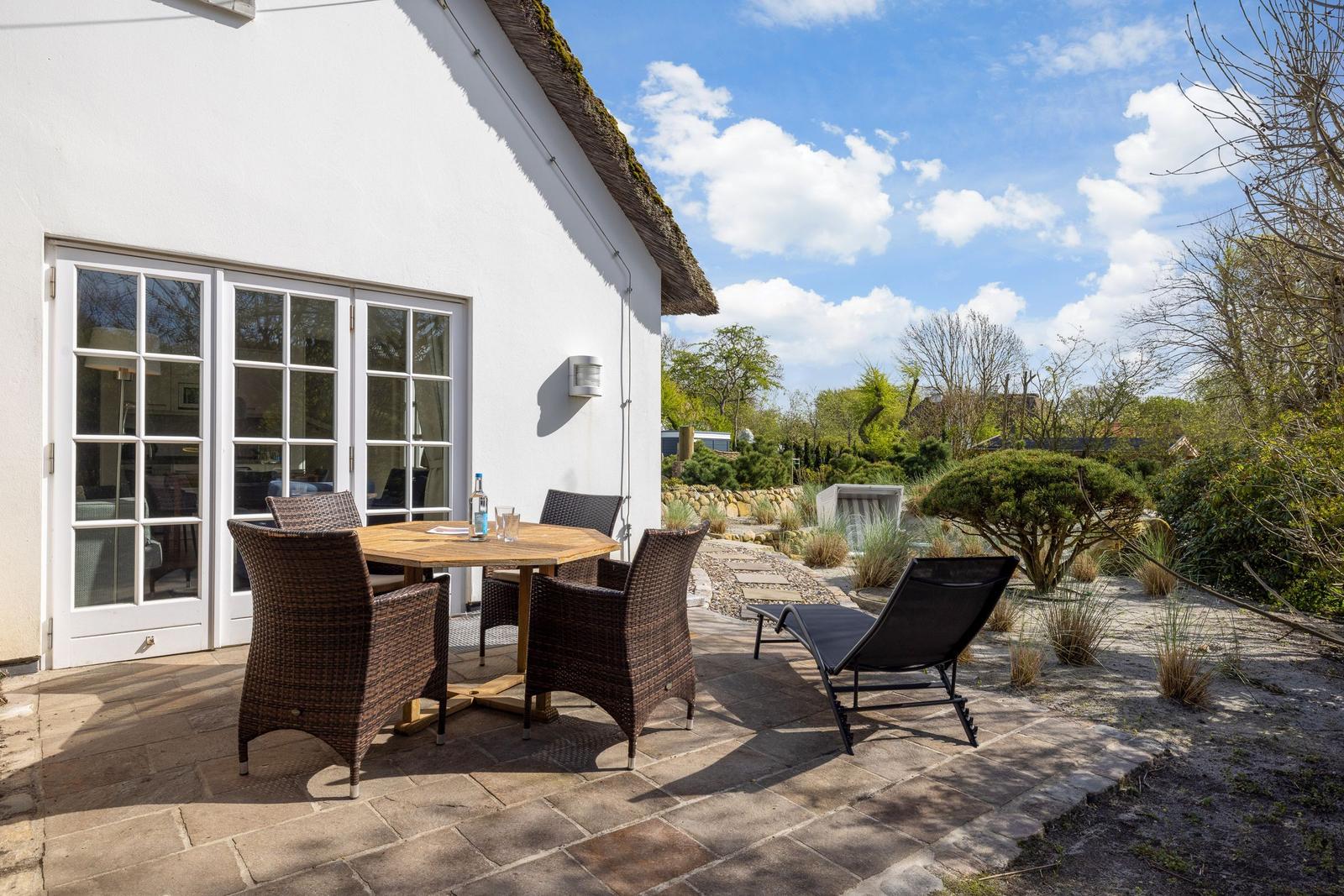 Terrace with table, chairs, and lounge chair. View into garden with trees and shrubs.