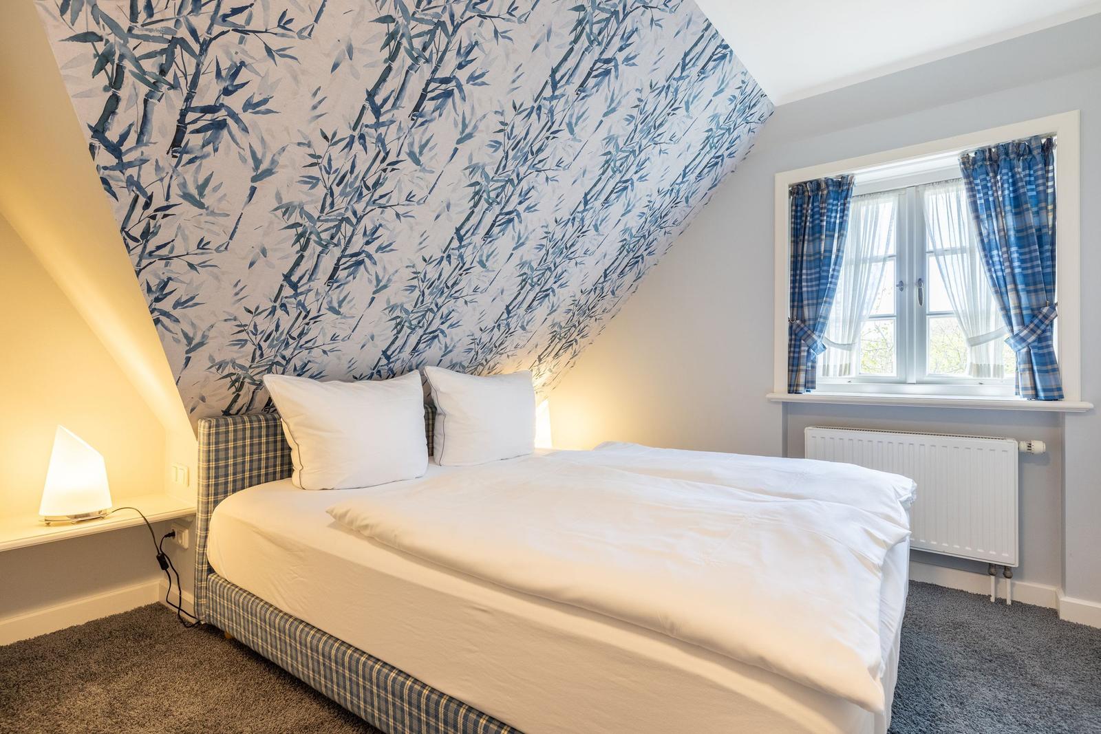 Bedroom with bed, wallpaper, and window with curtains.