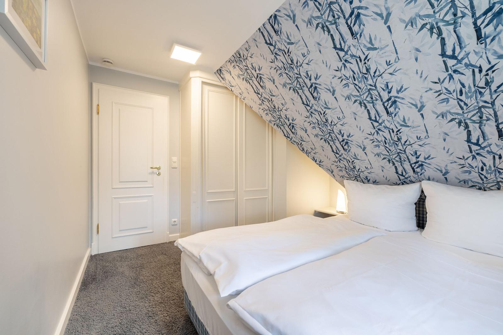 Bedroom with bed, wardrobe, and door. Wall with bamboo pattern.