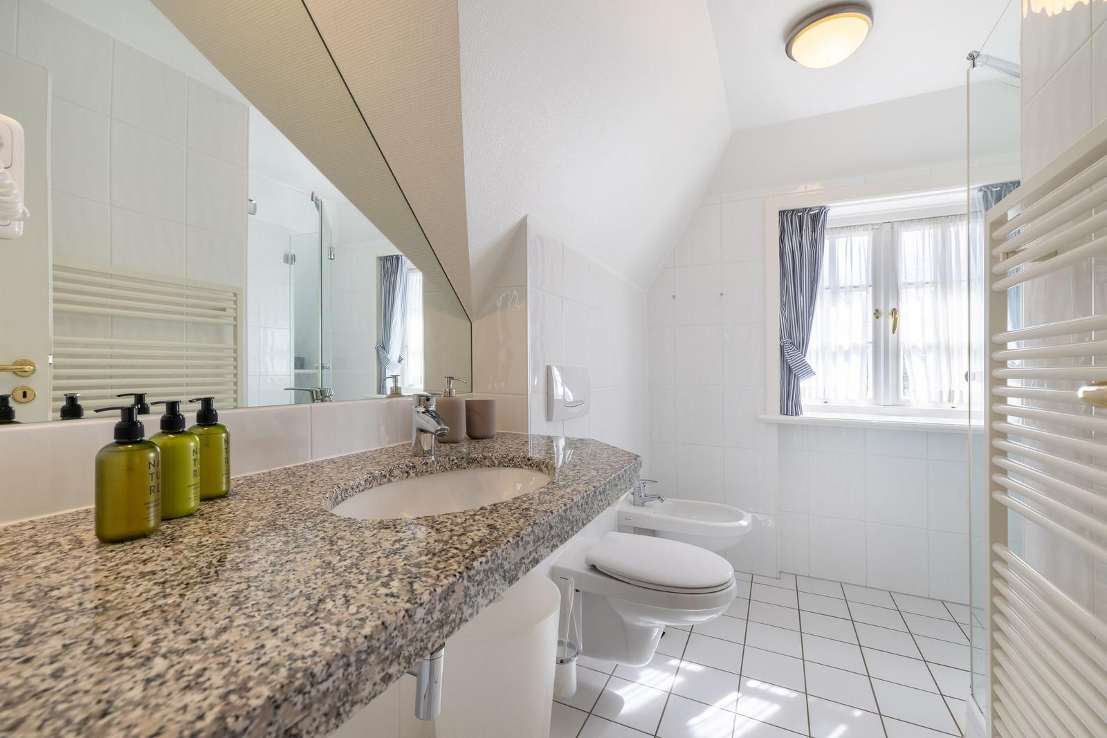 Bathroom with sink, toilet, and shower. Window with curtains.