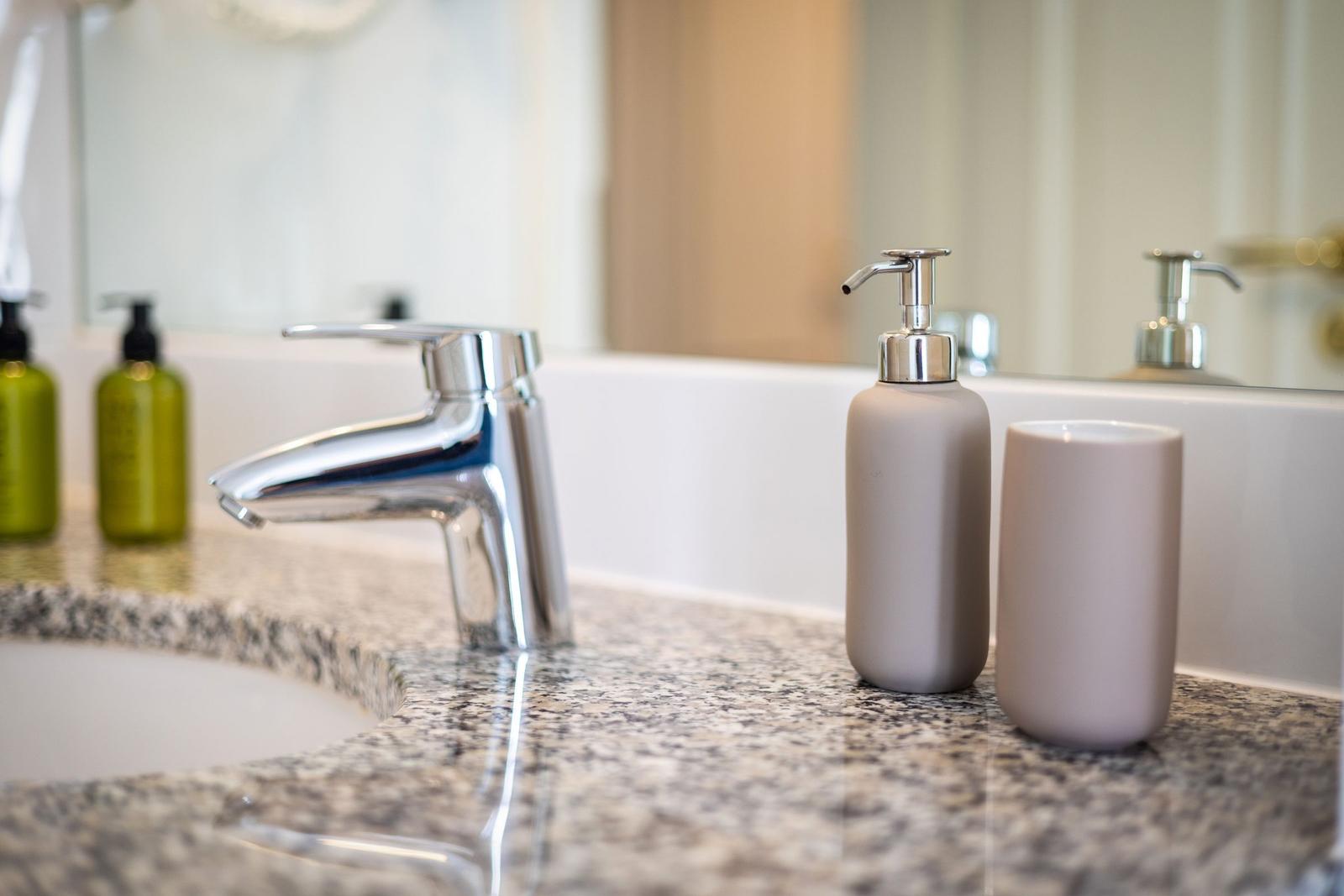 Sink with chrome faucet and soap dispenser on marble countertop.