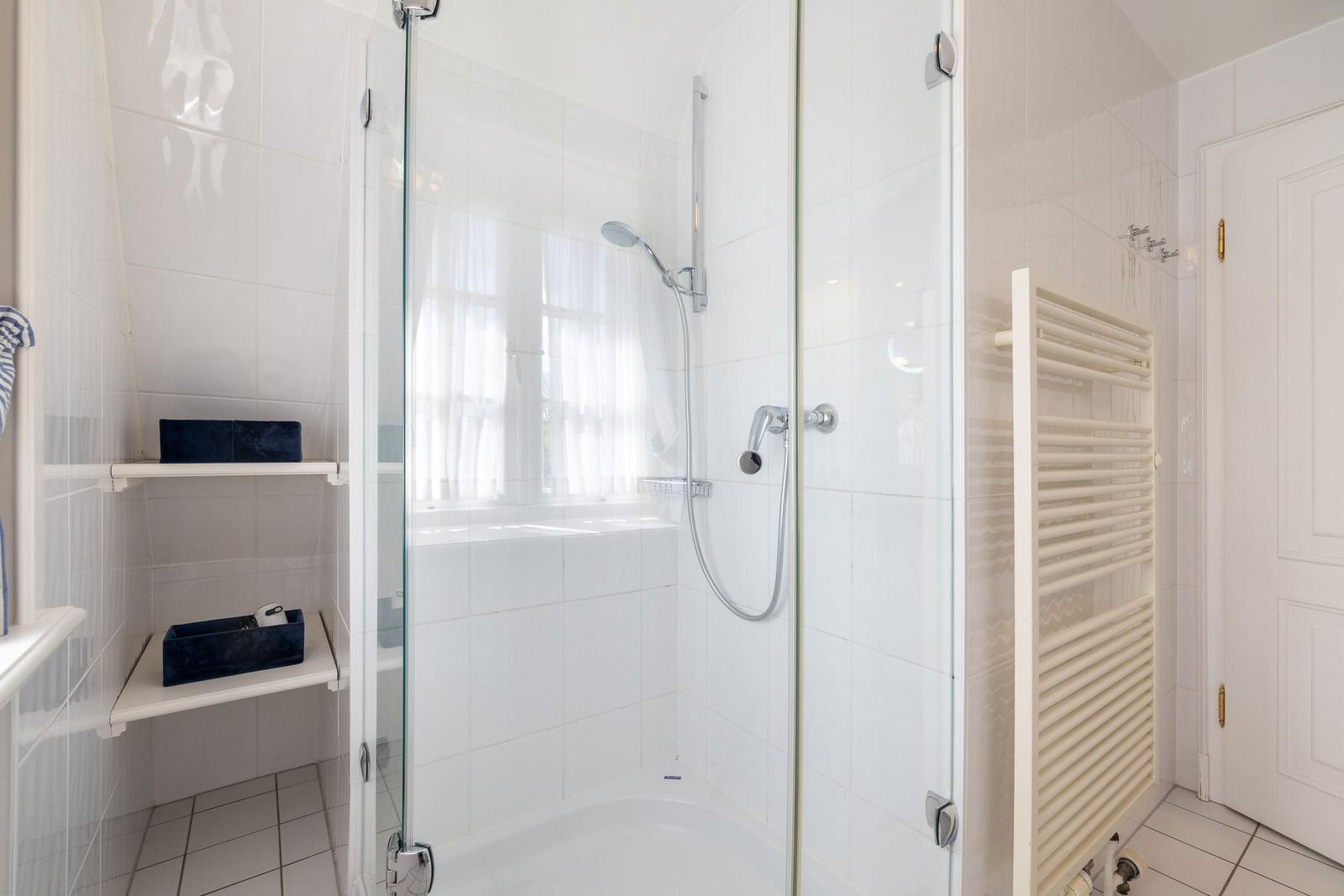 Shower enclosure with glass door, showerhead, and heater on the wall.
