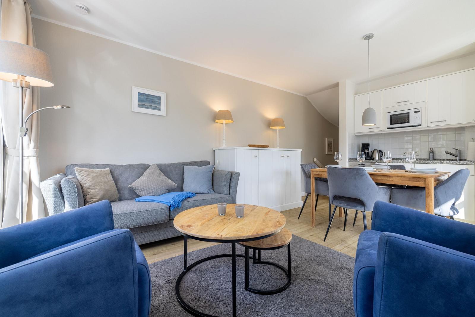Living room with sofa, armchairs, and dining table. Kitchen with microwave and worktop.