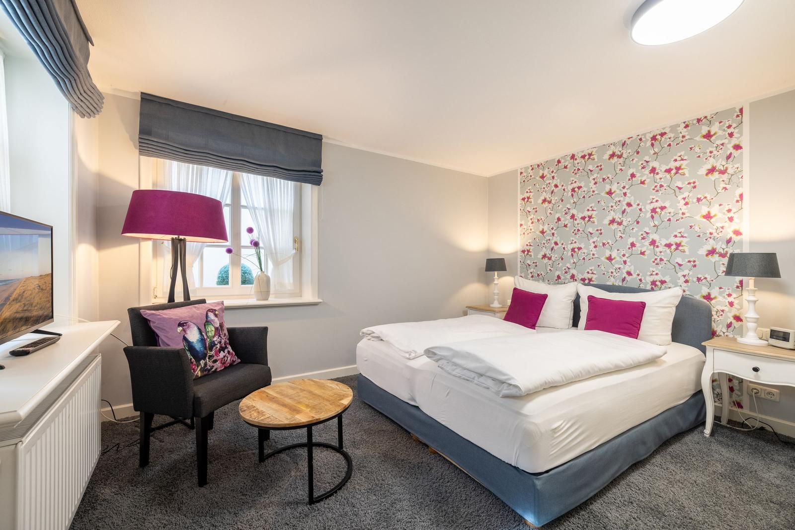 Bedroom with bed, armchair, and window. Wall with floral pattern.