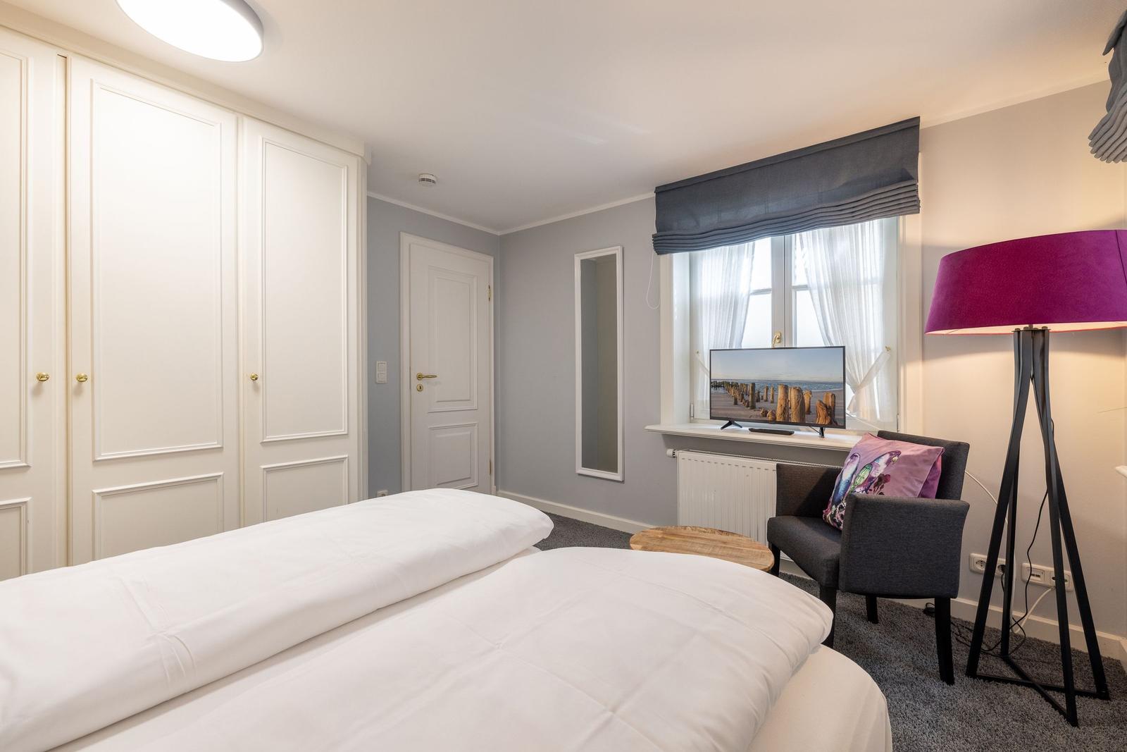 Bedroom with bed, wardrobe, armchair, and TV.