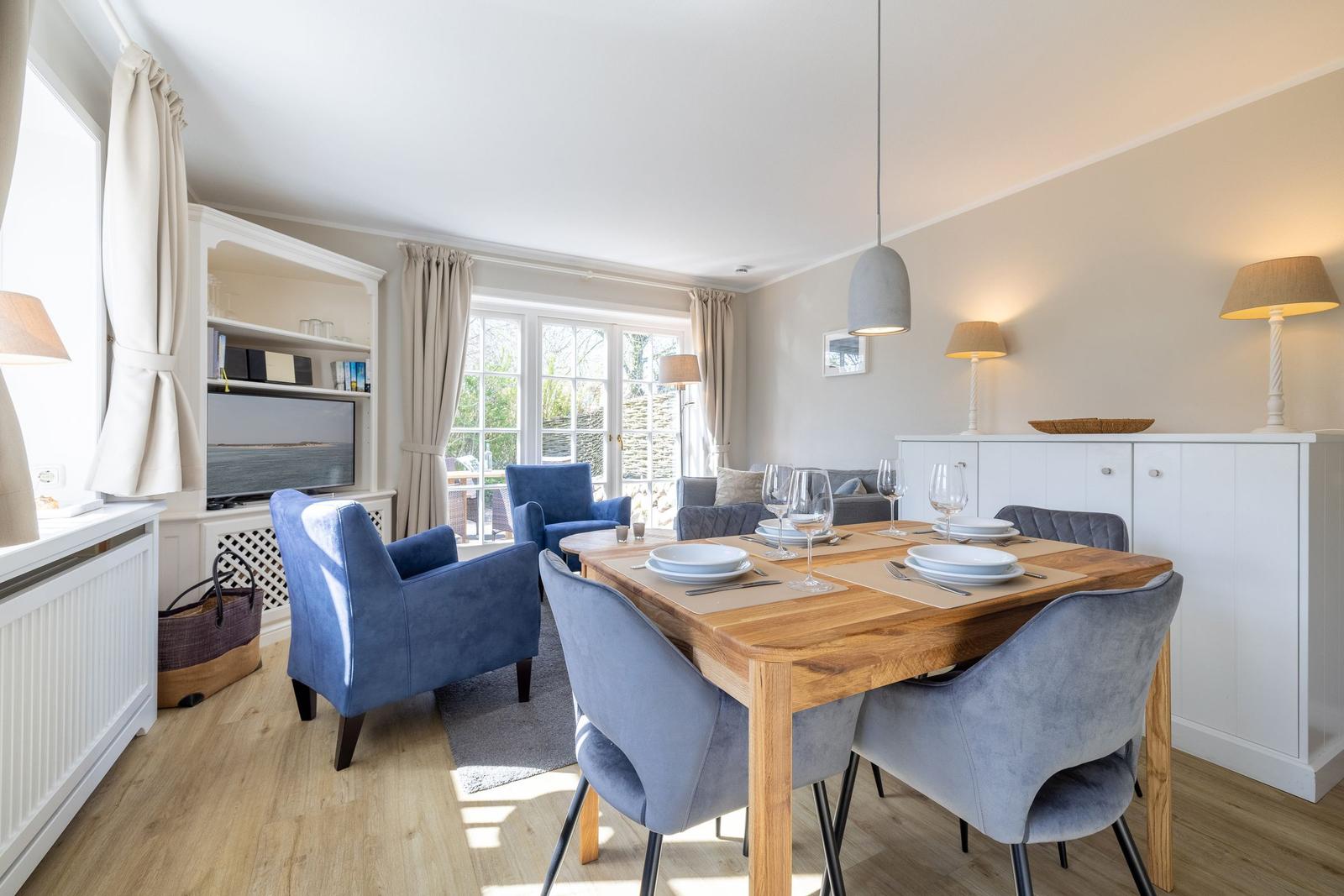 Dining area with wooden table, blue chairs, and window view. Living area with TV and seating.