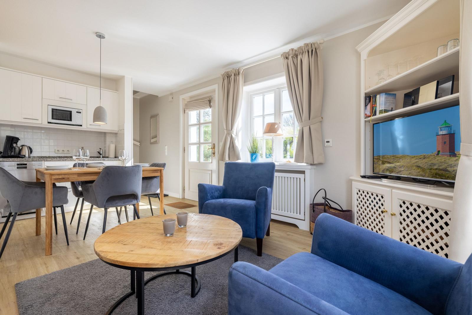 Living area with blue sofa, dining table, and kitchenette.