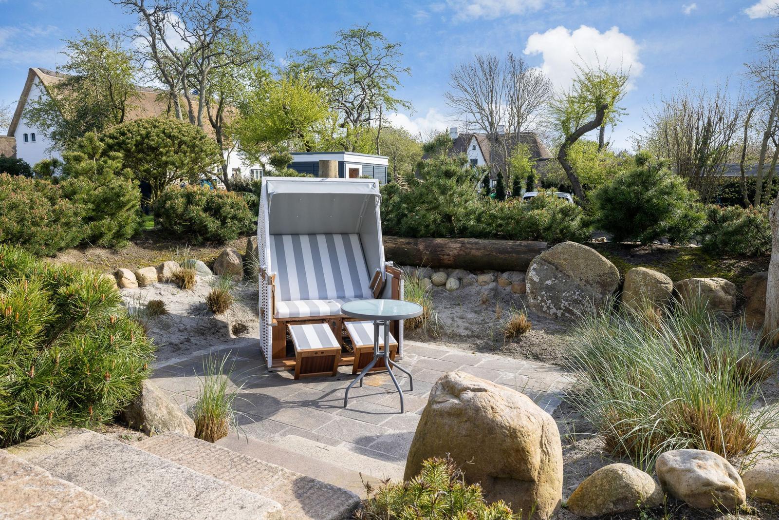 Garden with beach chair, table, and stones. Background: trees and houses.