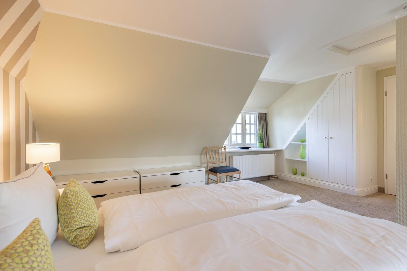 Bedroom with sloped ceiling, bed, wardrobe, and window.