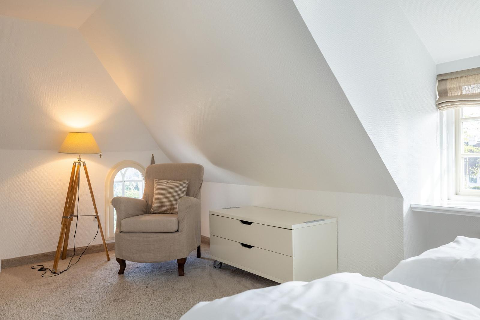 Bedroom with sloped ceiling, armchair, dresser, and window.