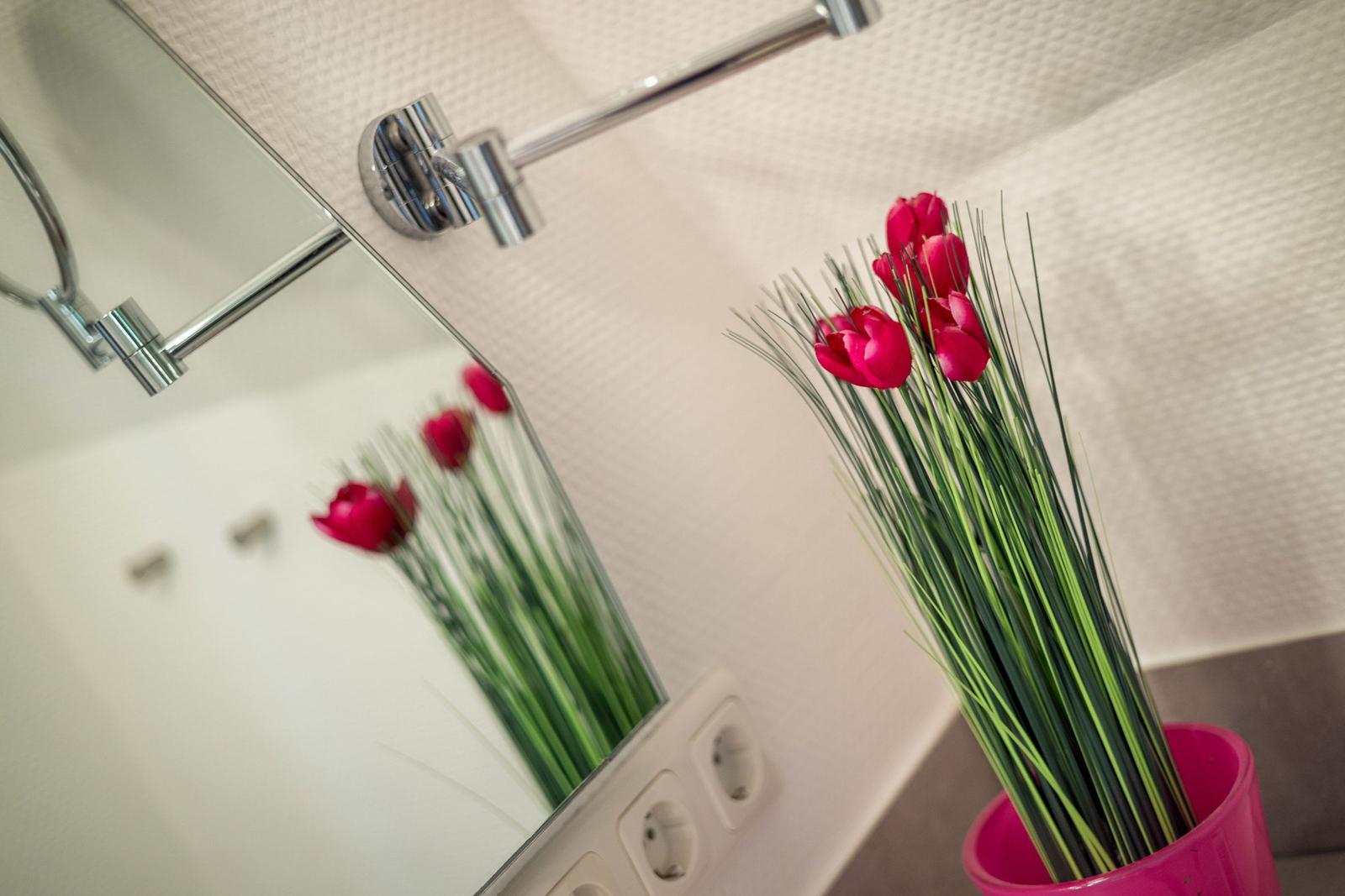 Mirror reflects red tulips in a pink vase.