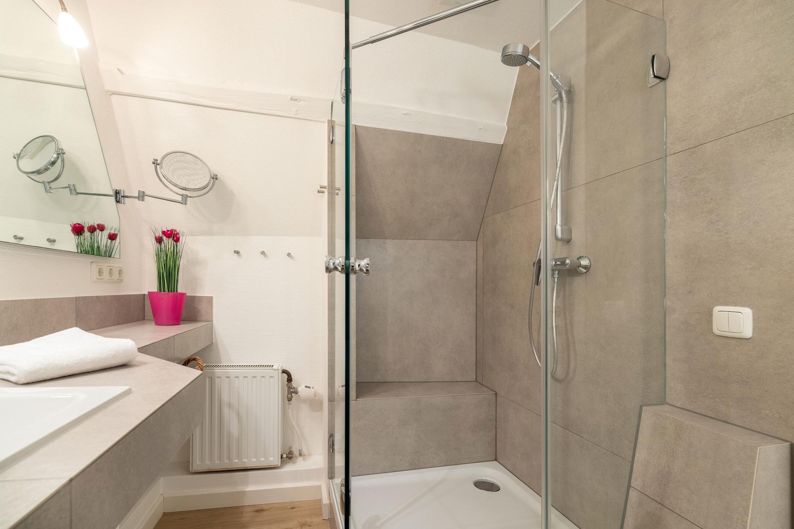 Bath with shower, sink, and mirror. A pink pot with tulips sits on the countertop.