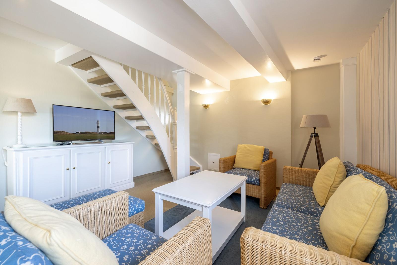 Living room with sofa, armchair, and TV under a staircase.