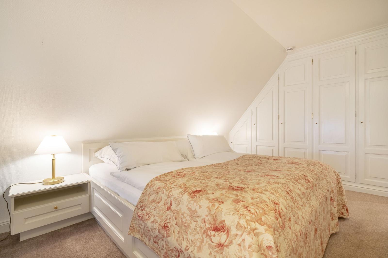 Bedroom with double bed, nightstand, and wardrobe under sloped ceiling.