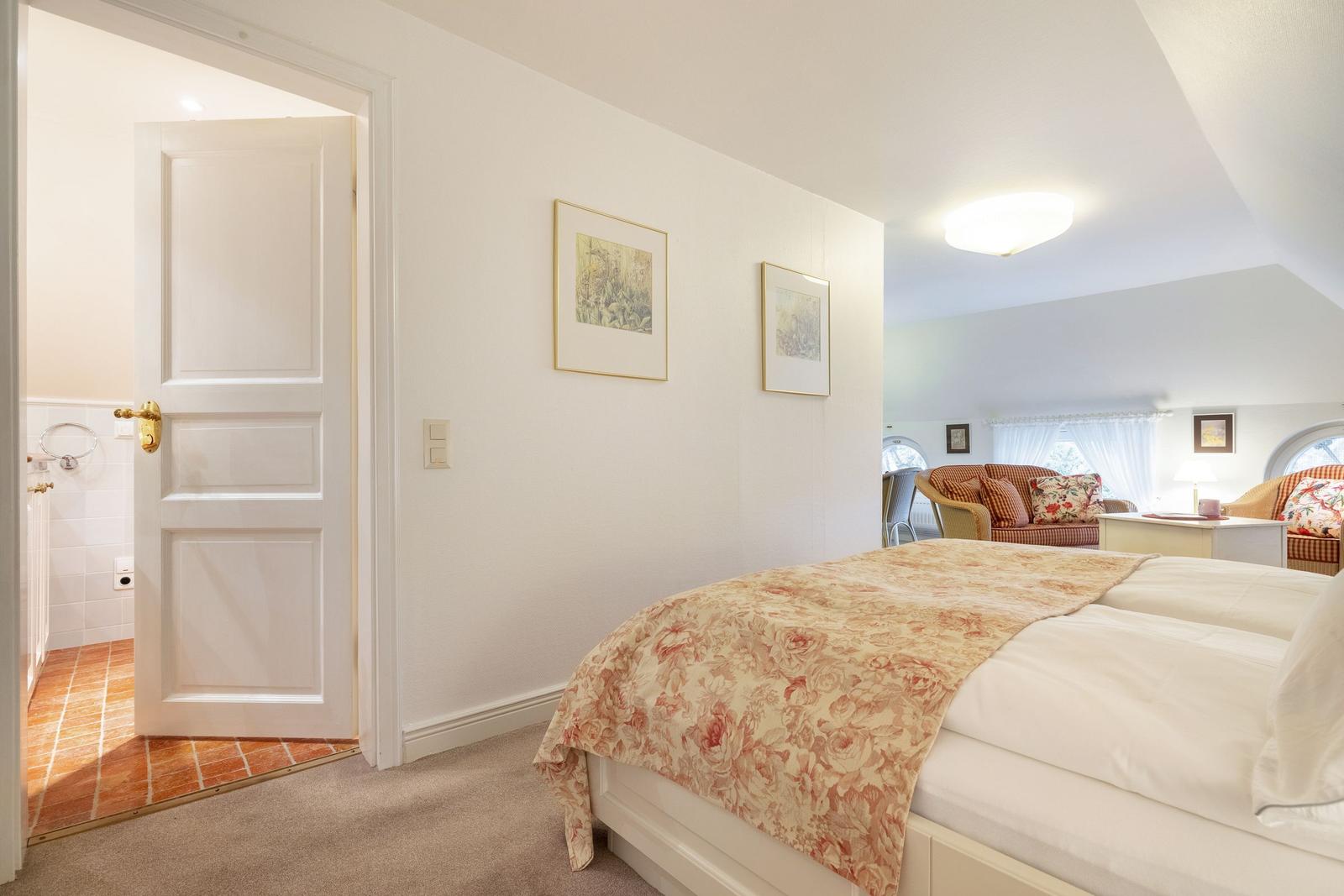 Bedroom with bed, door to bathroom, and view into living area.