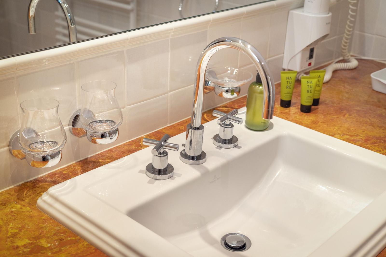 Sink with chrome faucet and green bottles on marble countertop.