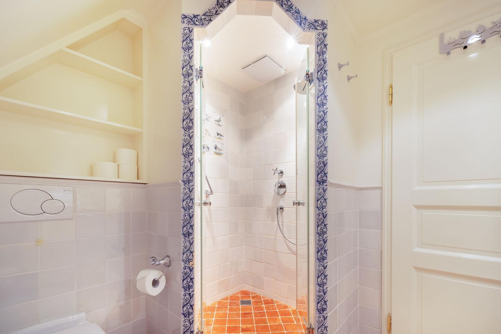 Bathroom with shower, toilet, and shelf. Shower area with glass door and blue patterned frame.