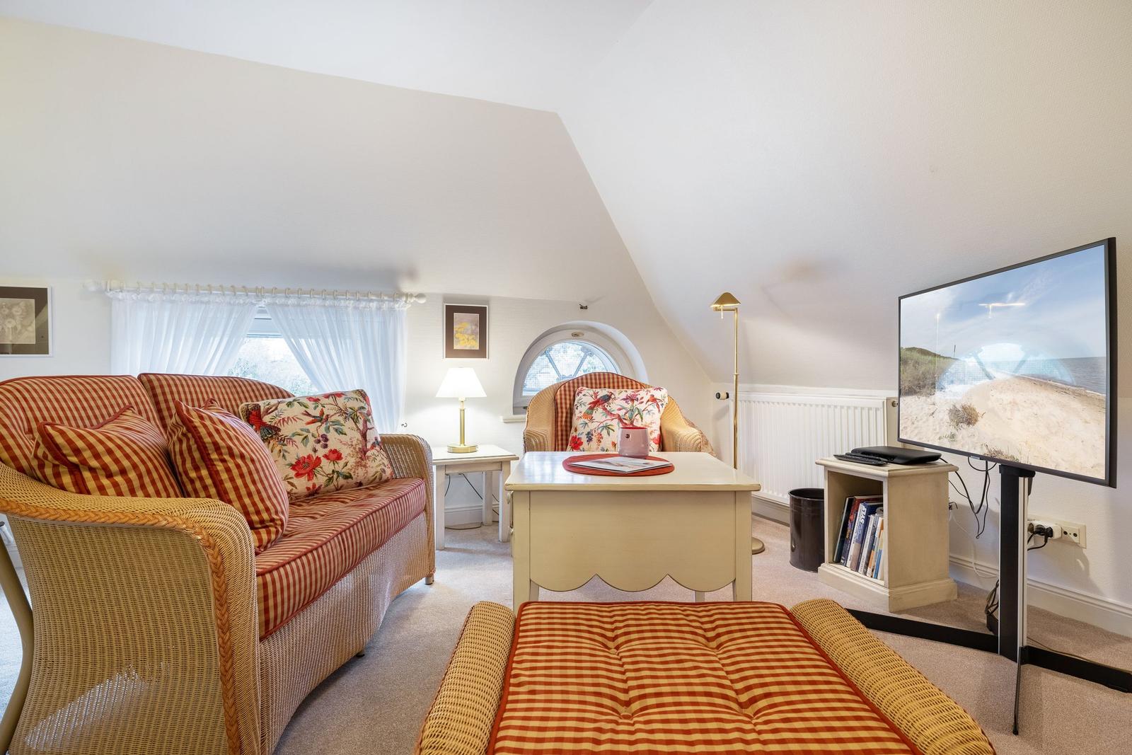 Living room with sofa, armchair, and TV under sloped ceiling