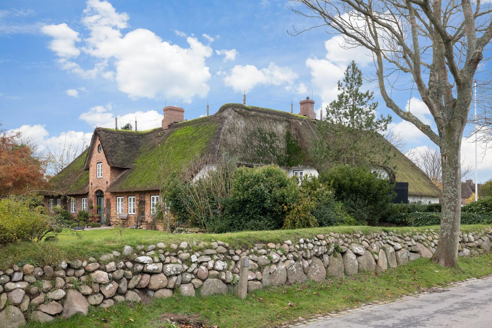 Traditional house with green roof, stone wall, and trees in the front garden.