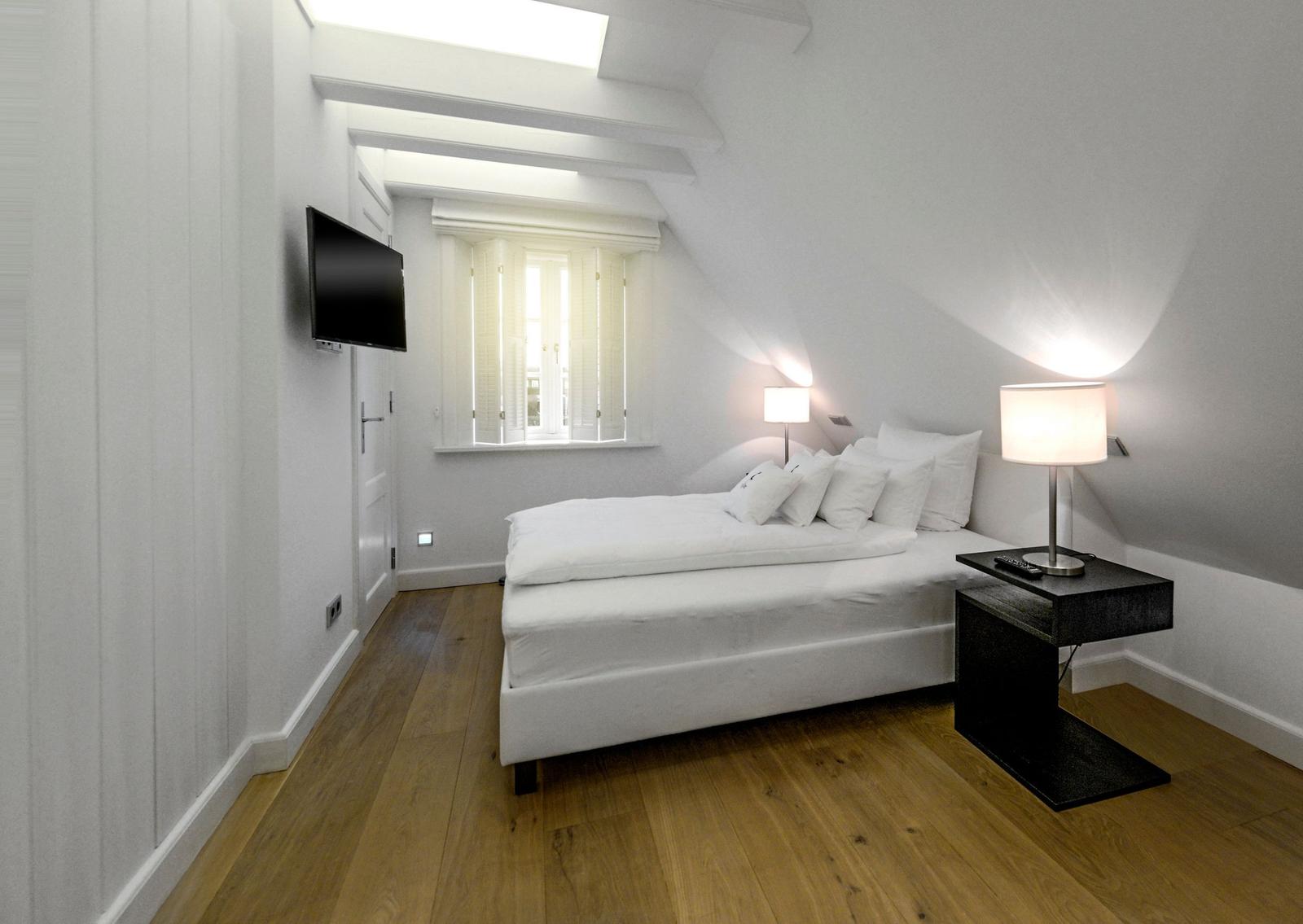 Schlafzimmer mit Dachbodenfenster, Bett, Nachttisch und Wand-TV.