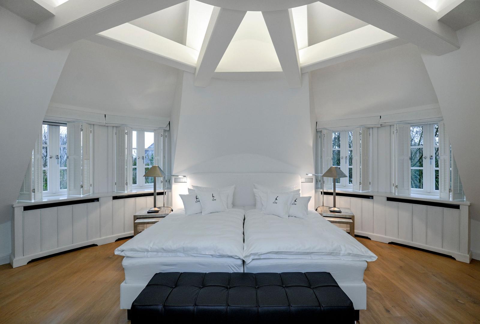 Schlafzimmer mit Doppelbett, weißen Fenstern und Holzboden.