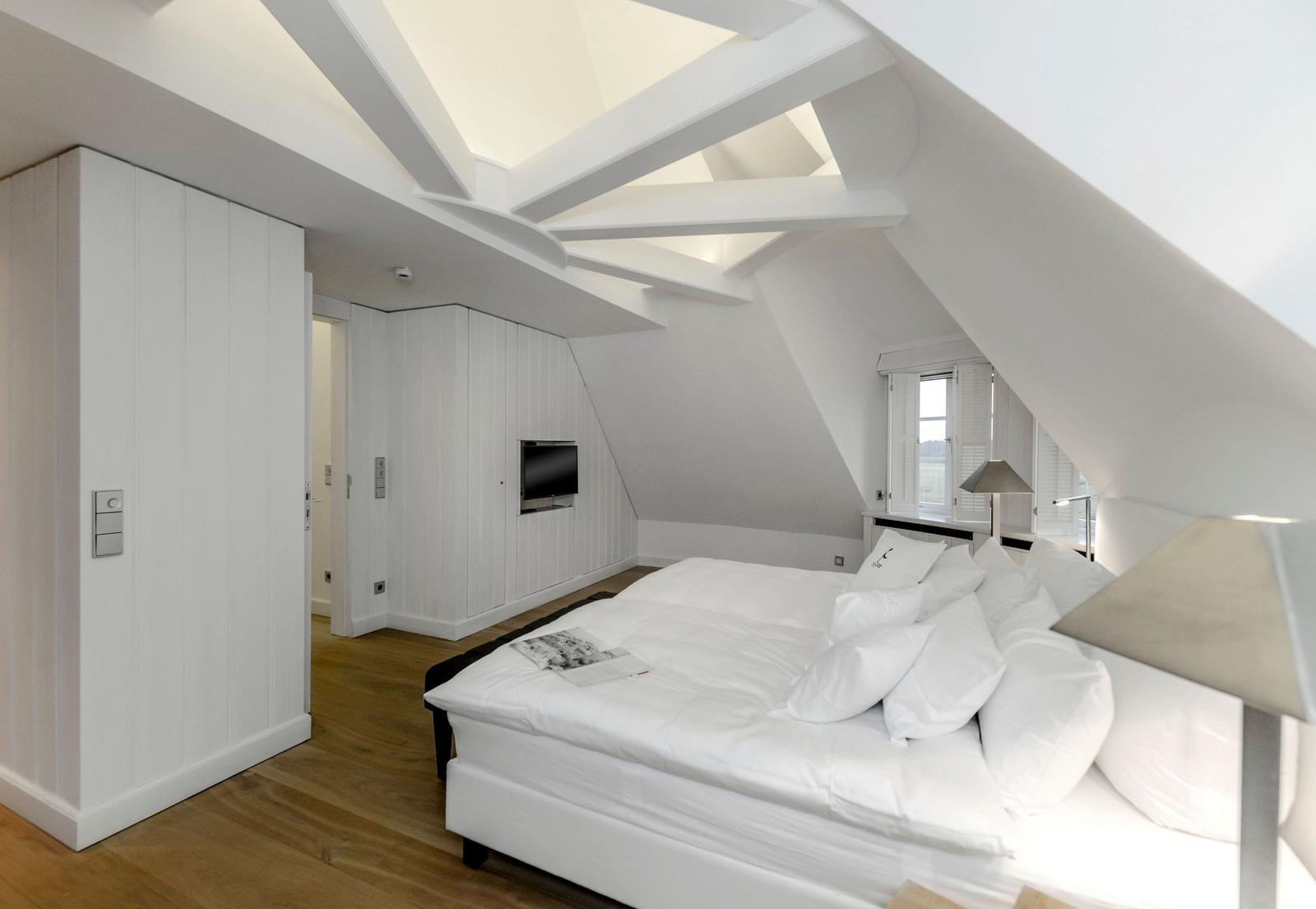 Schlafzimmer mit Dachschrägen, weißem Bett und Holzboden.