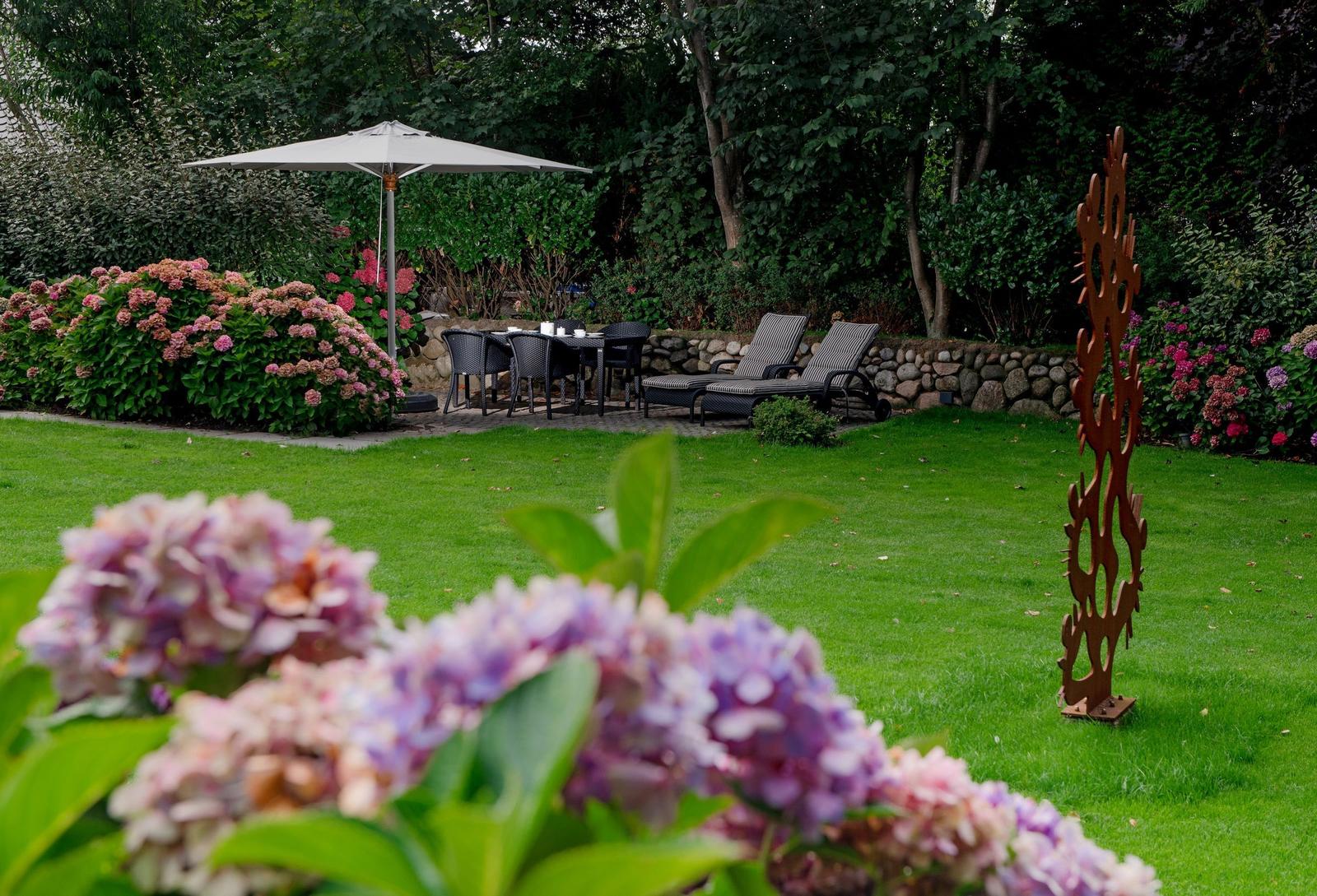 Garten mit Sonnenschirm, Sitzgruppe und Blumenbeeten.