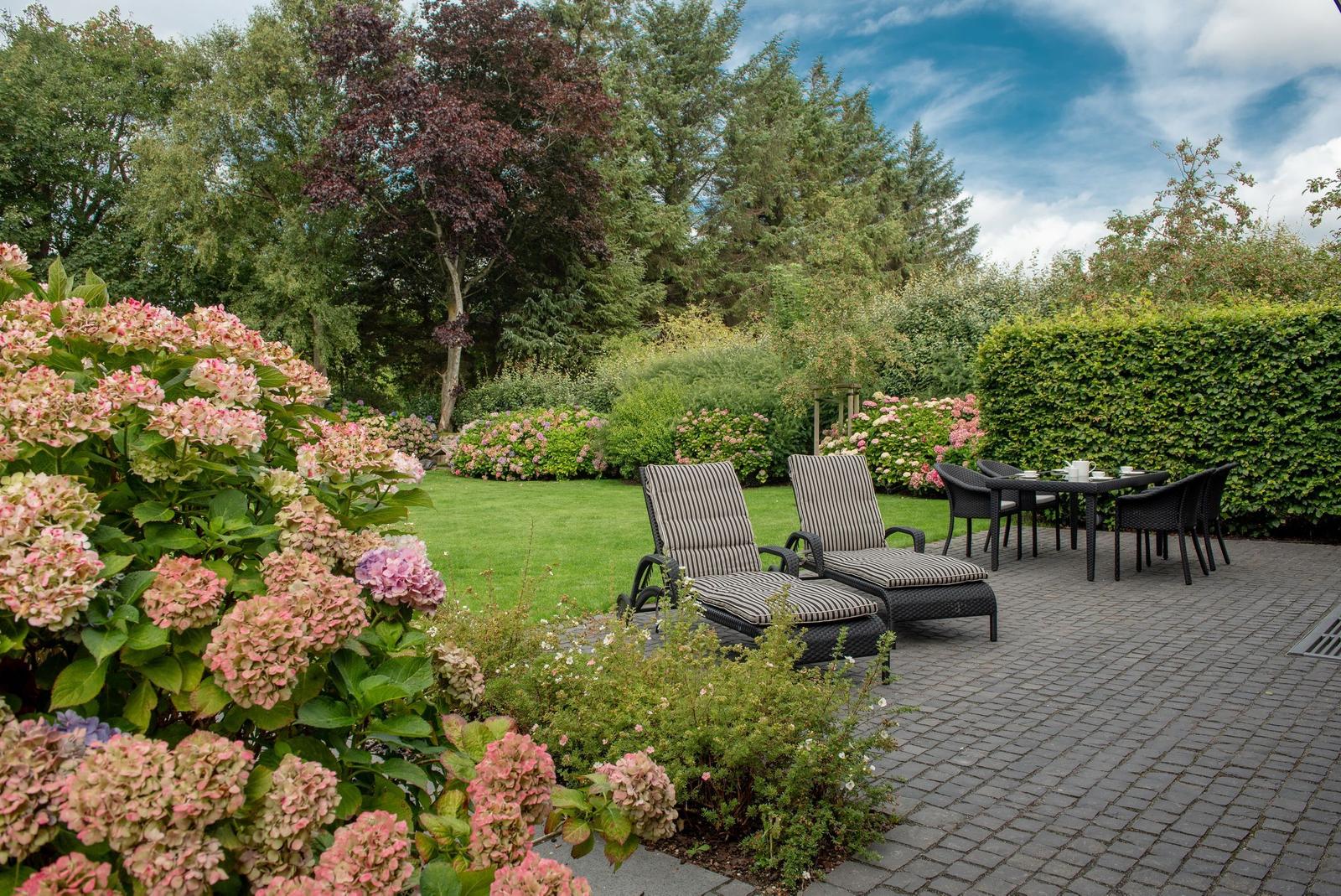 Garten mit Sitzgelegenheiten und Blumenbeeten auf gepflastertem Platz.